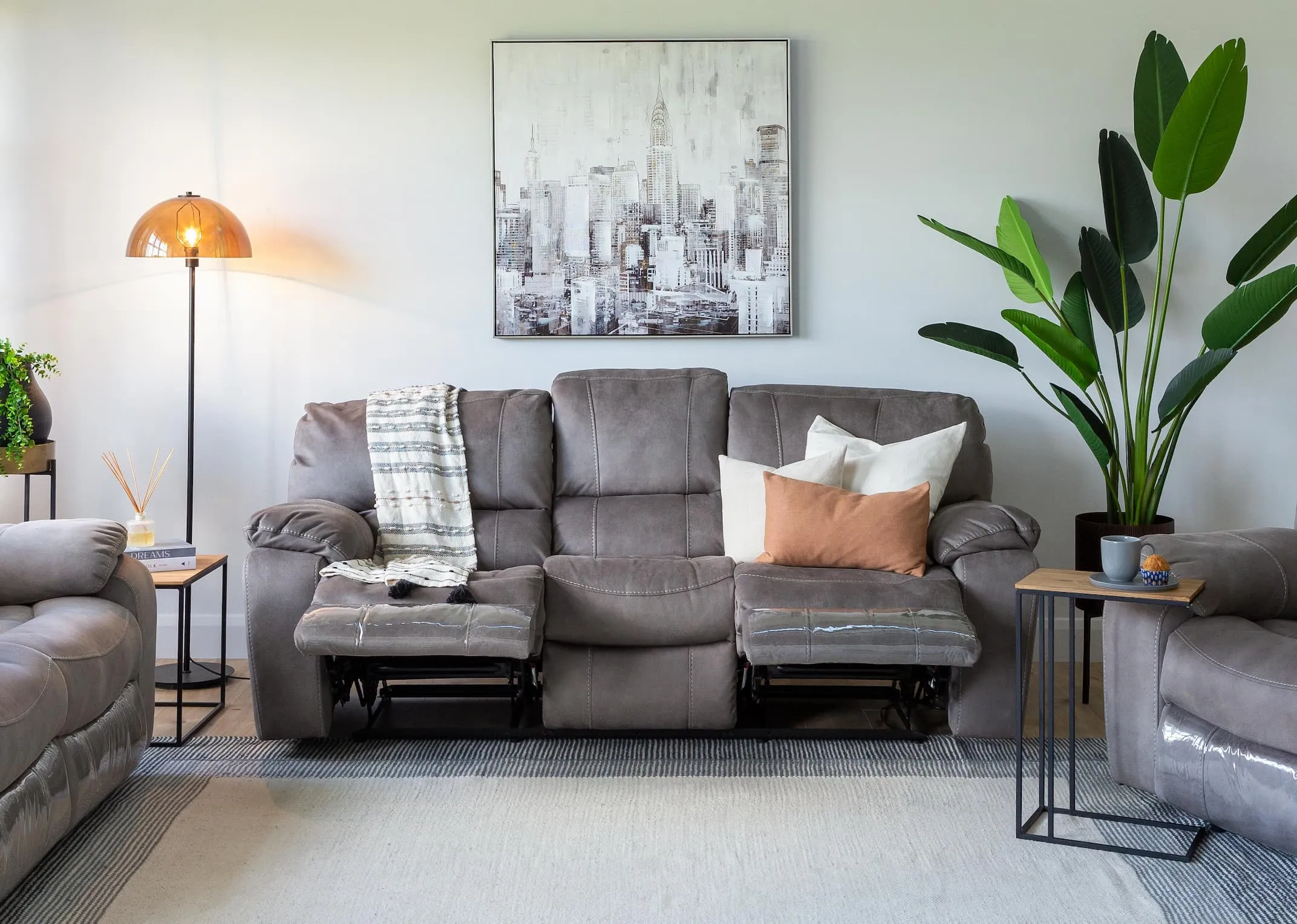 A lifestyle image of the Bradford grey 3 seater sofa reclined with the Aston tables & Mellan floor lamp.