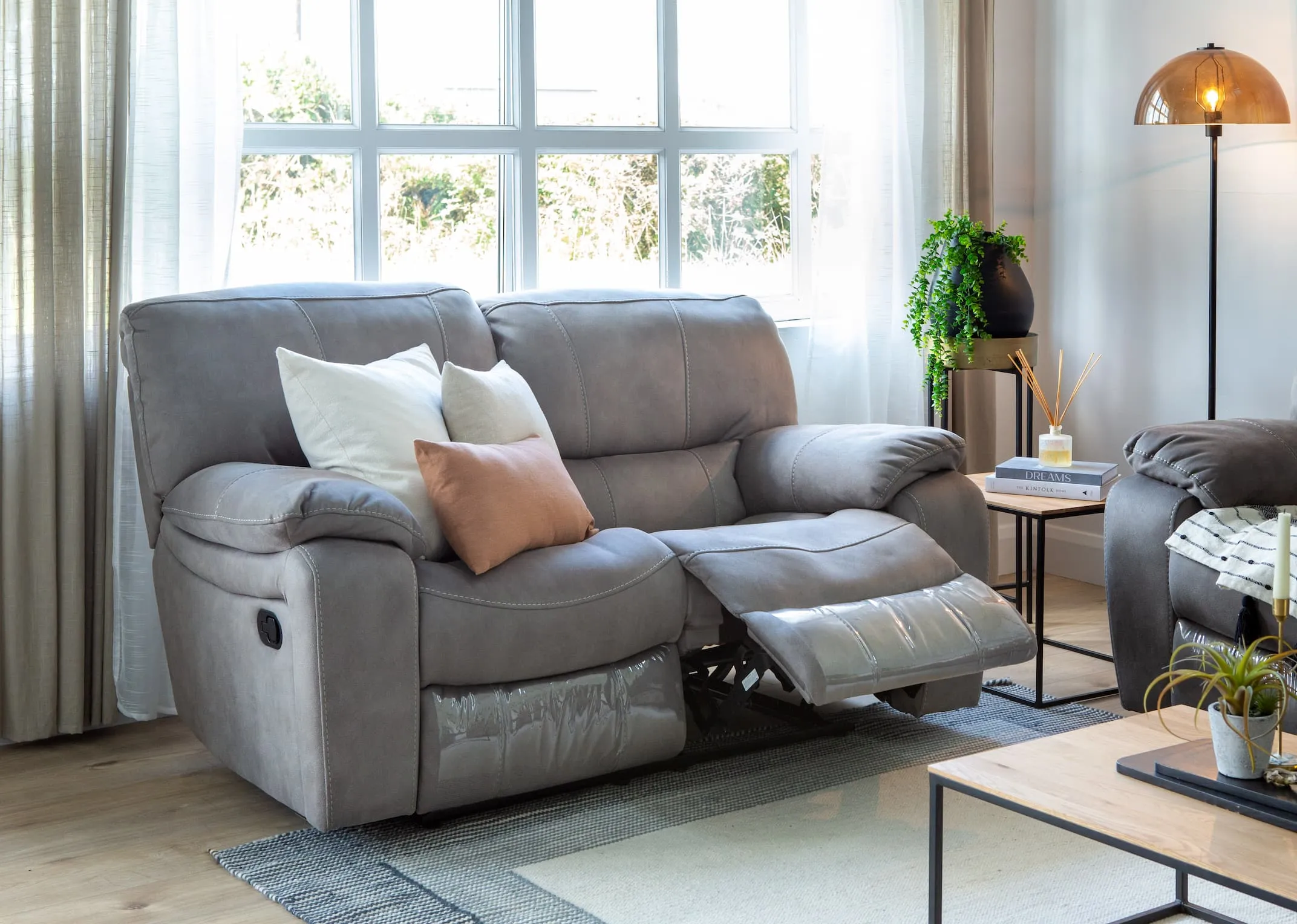 A lifestyle image of the Bradford grey 2 seater sofa reclined with the Aston tables & Mellan floor lamp.