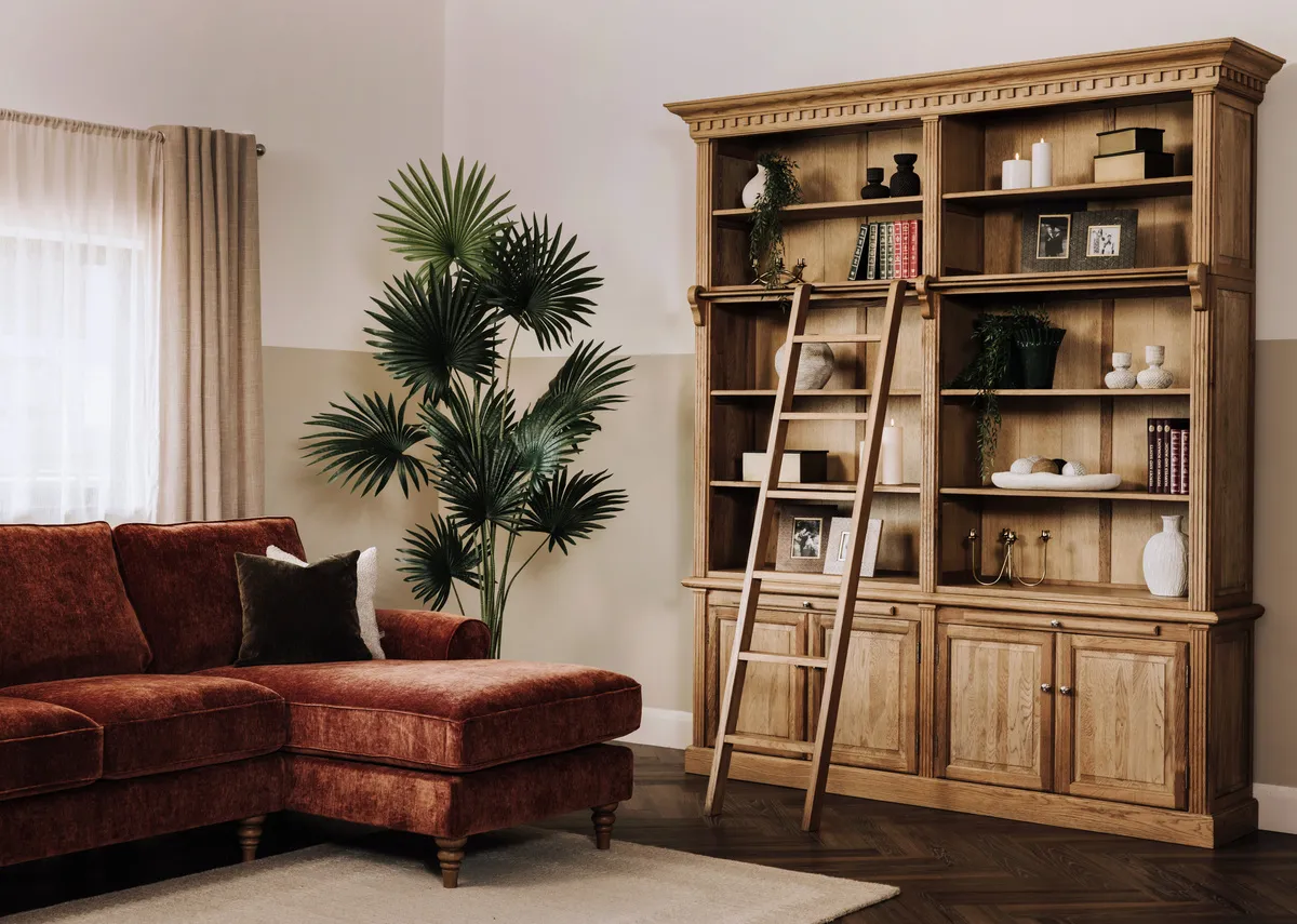 A lifestyle image of the Iona Bookacse with ladder with shelves filled with books and accessories with the Cotswold chaise.