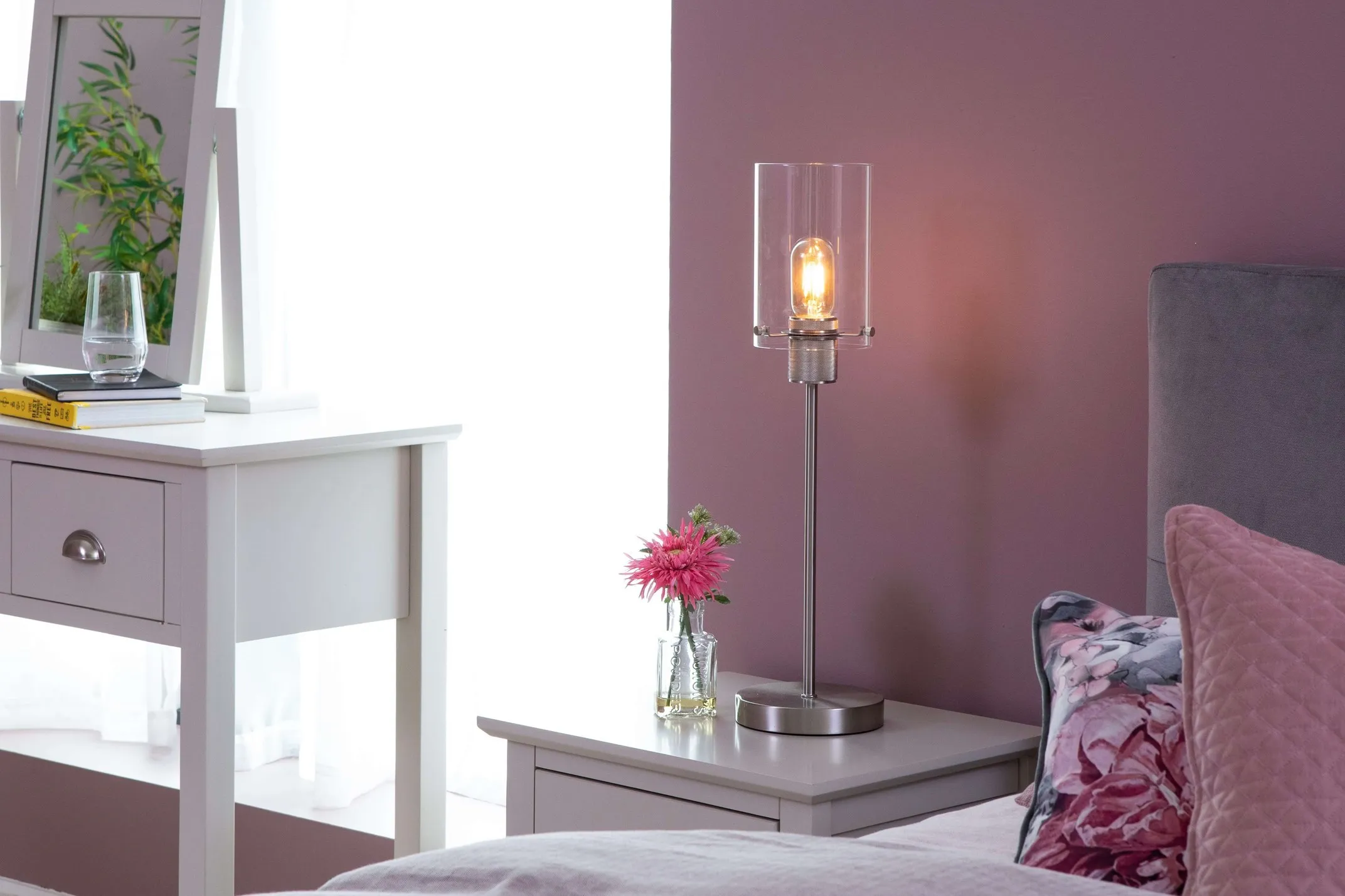 A lifestyle image of the Karina Chrome table lamp with a bedstand and pink decor