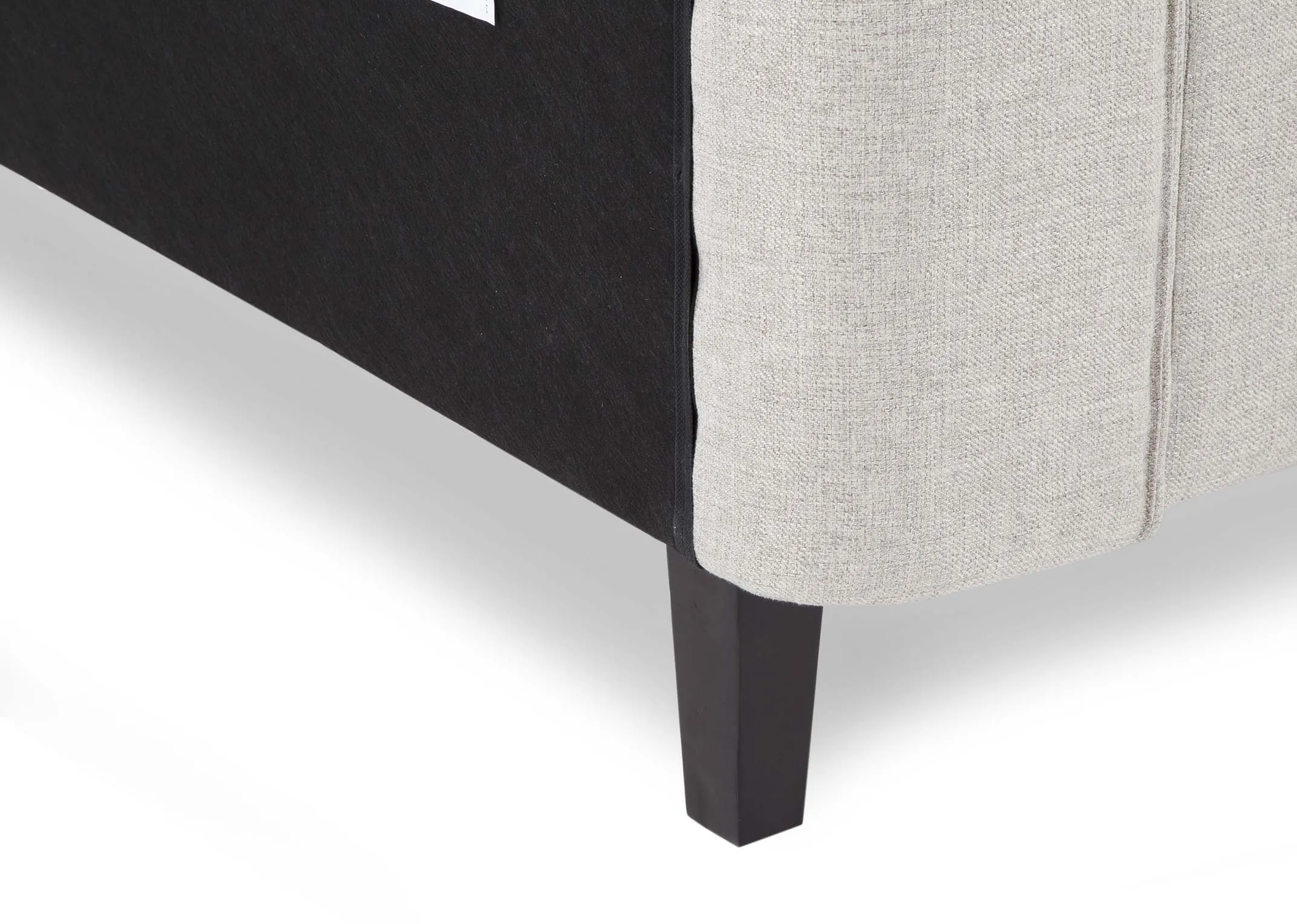 A close up view of the leg on the 5 ft beige fabric Chelsea bedframe