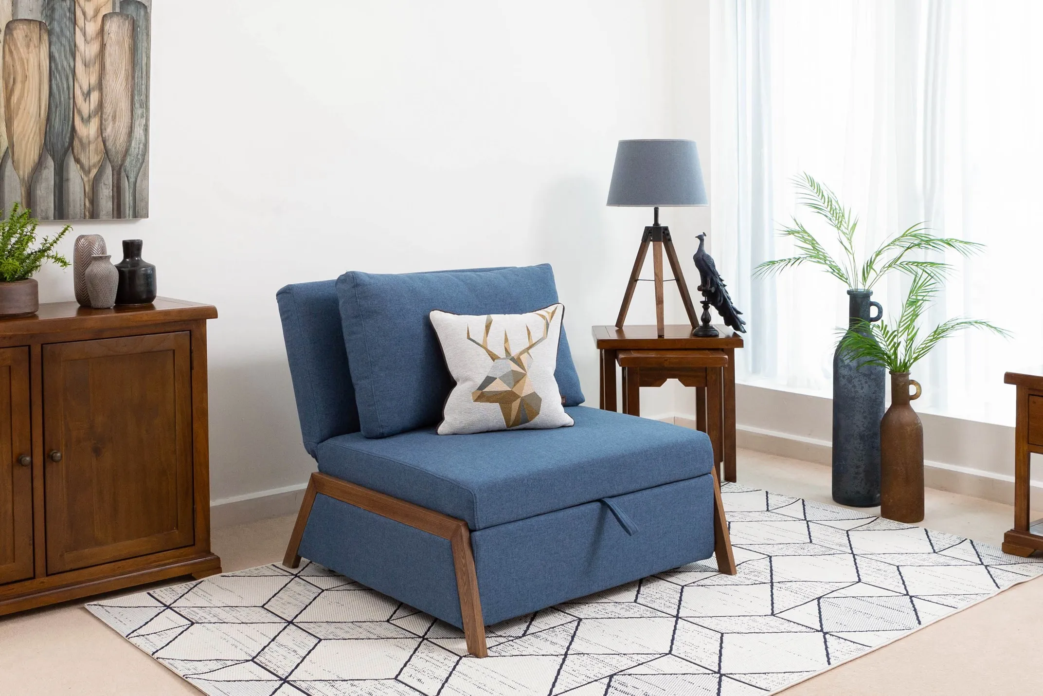 A lifestyle image of the blue fabric 1 seater Theo sofabed featuring the Holly lamp and the Aisling nests of tables