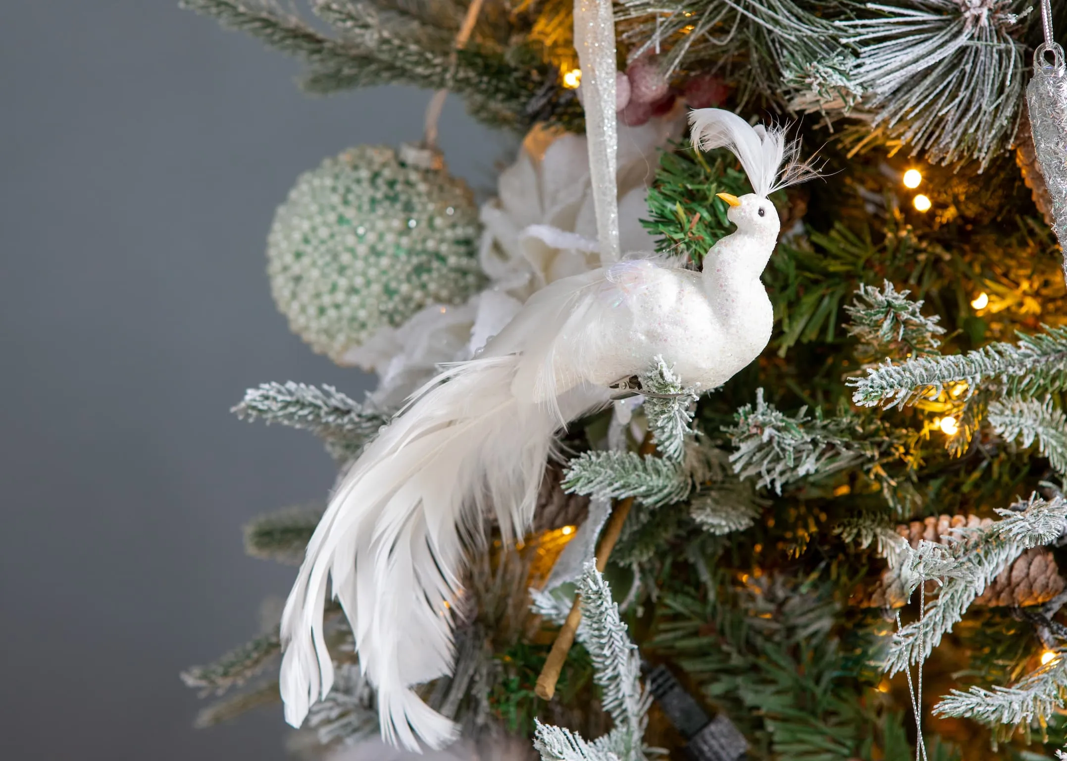A lifestyle image of the white bird 25cm with feathers & Xmas spray on Christmas tree.