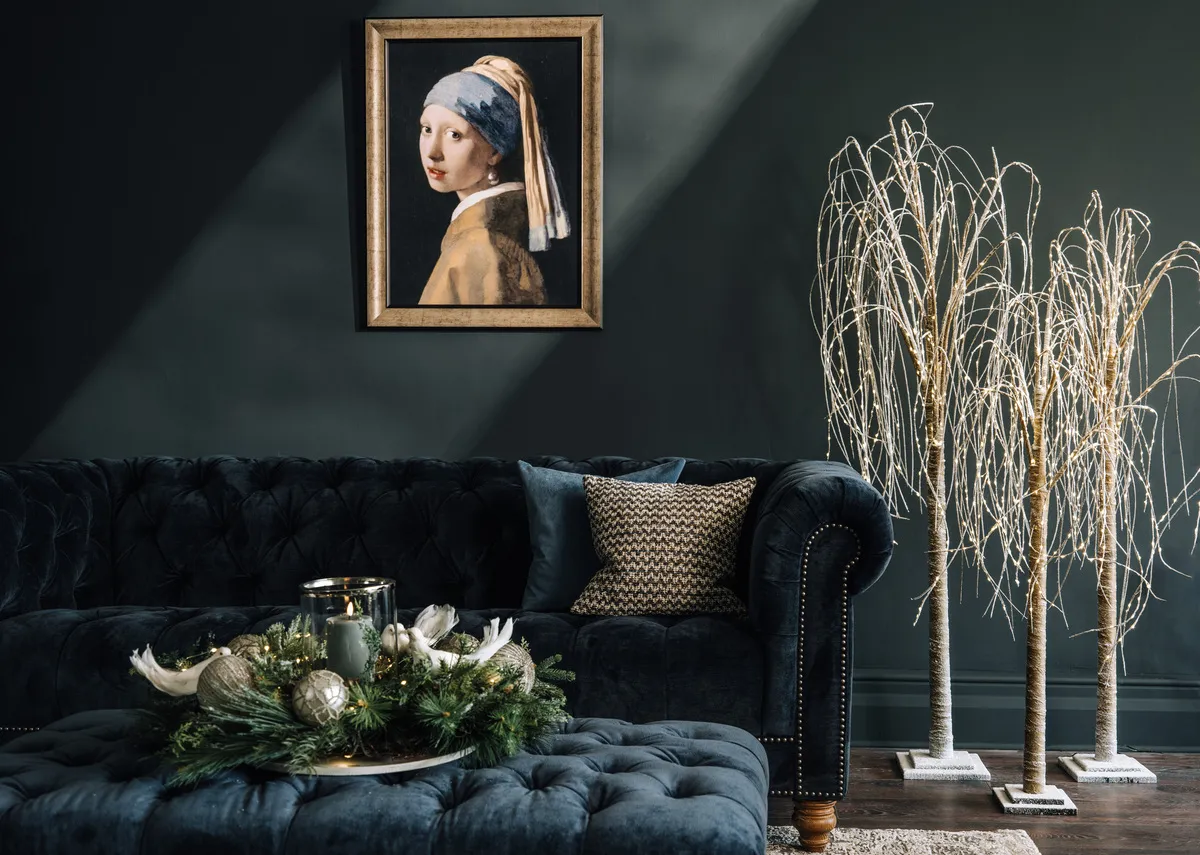 A lifestyle image of the Adare 3.5 seater in  navy velvet with Willow trees in all sizes and Girl with a Pearl earring picture.