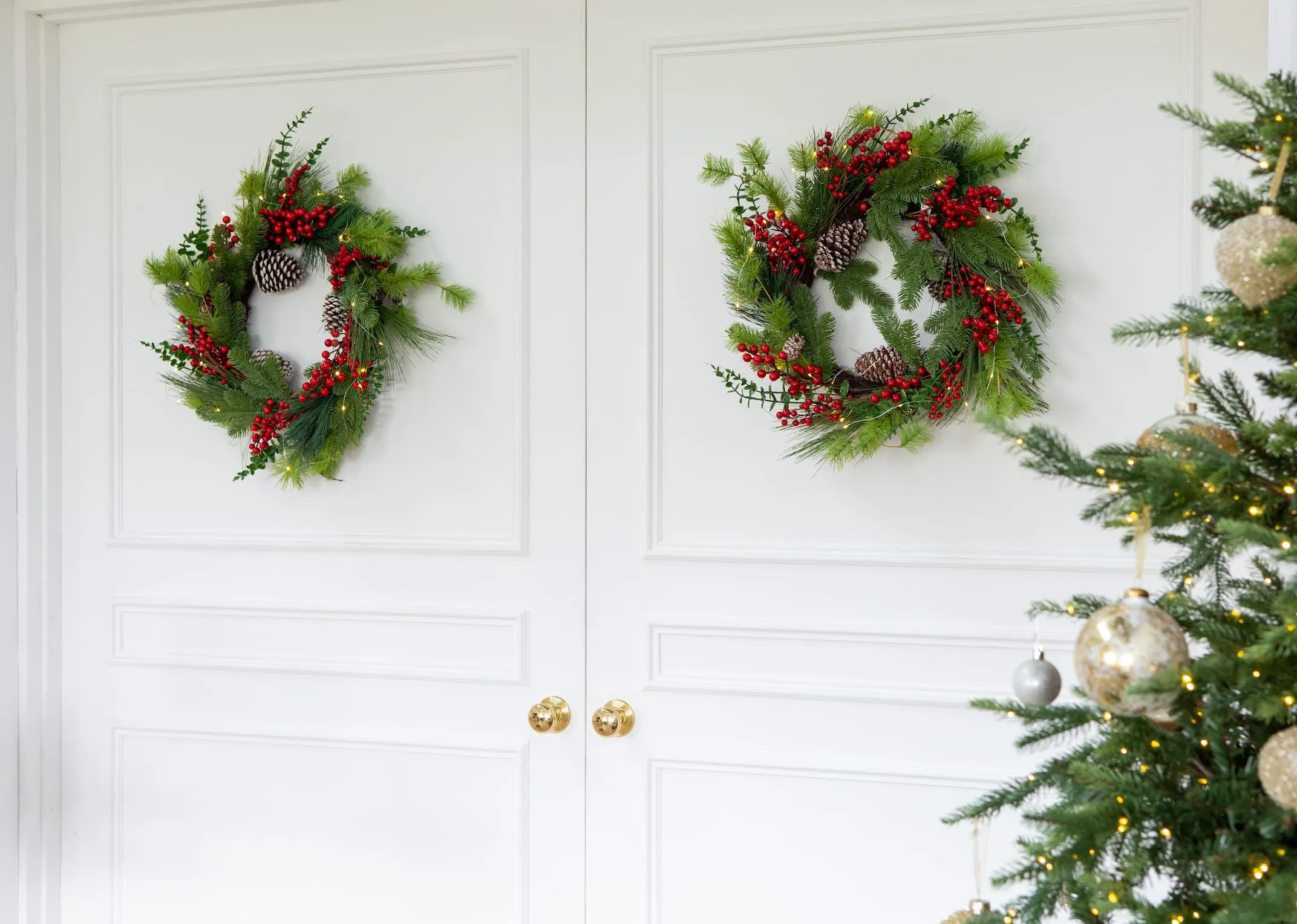 A lifestyle image of 2 berry & pine wreaths hanging on a set of double doors