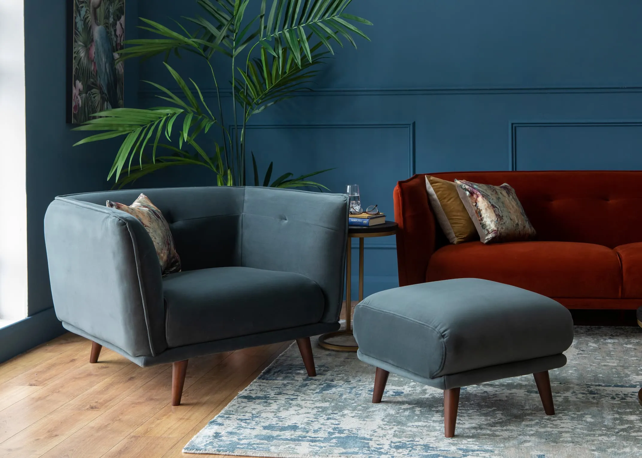 A lifestyle image of the Girona Grey Armchair with footstool & Rust velvet sofa.