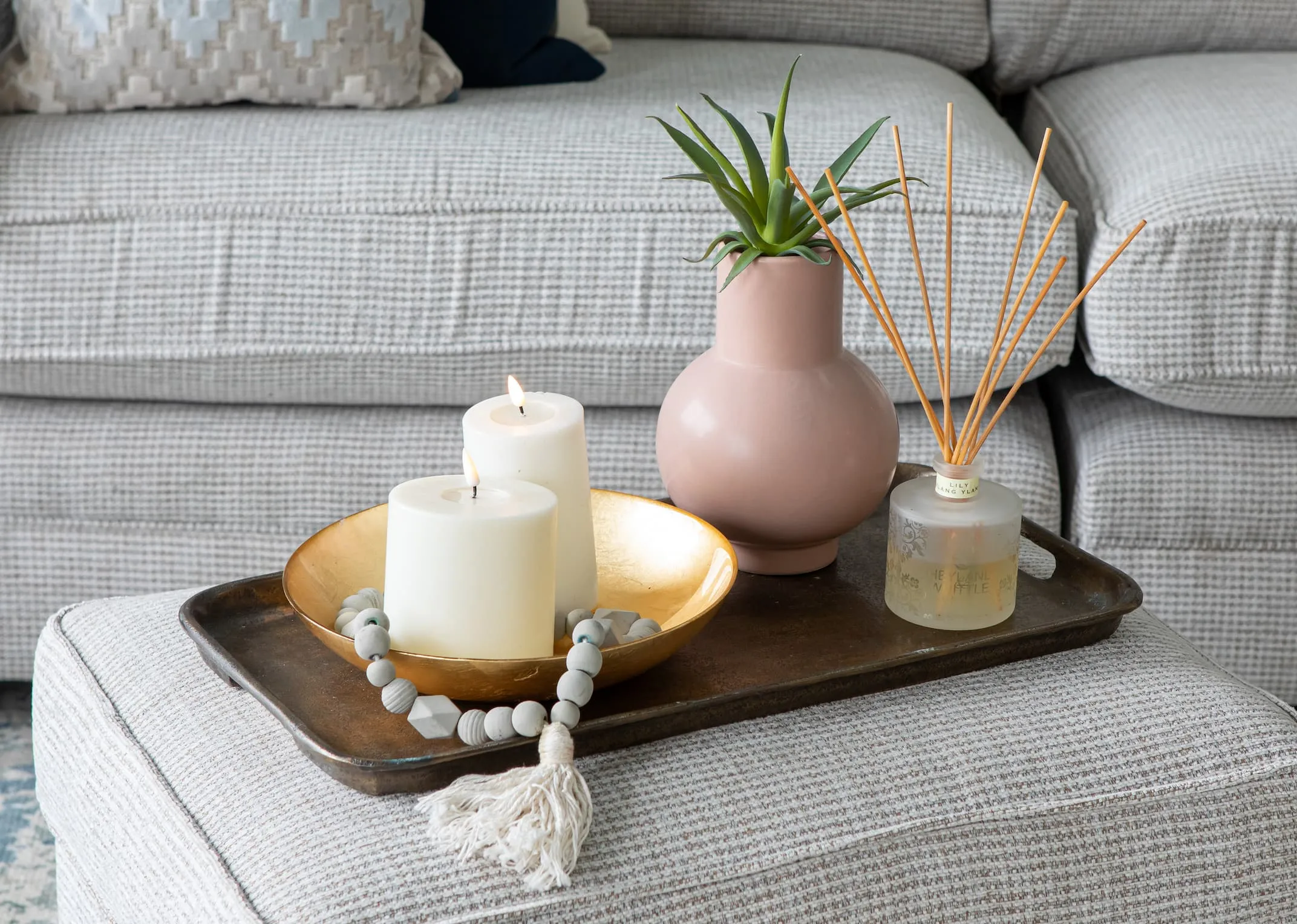 A lifestyle image of the Strata sofa & footstool with tray & cassia vase and real flame candles