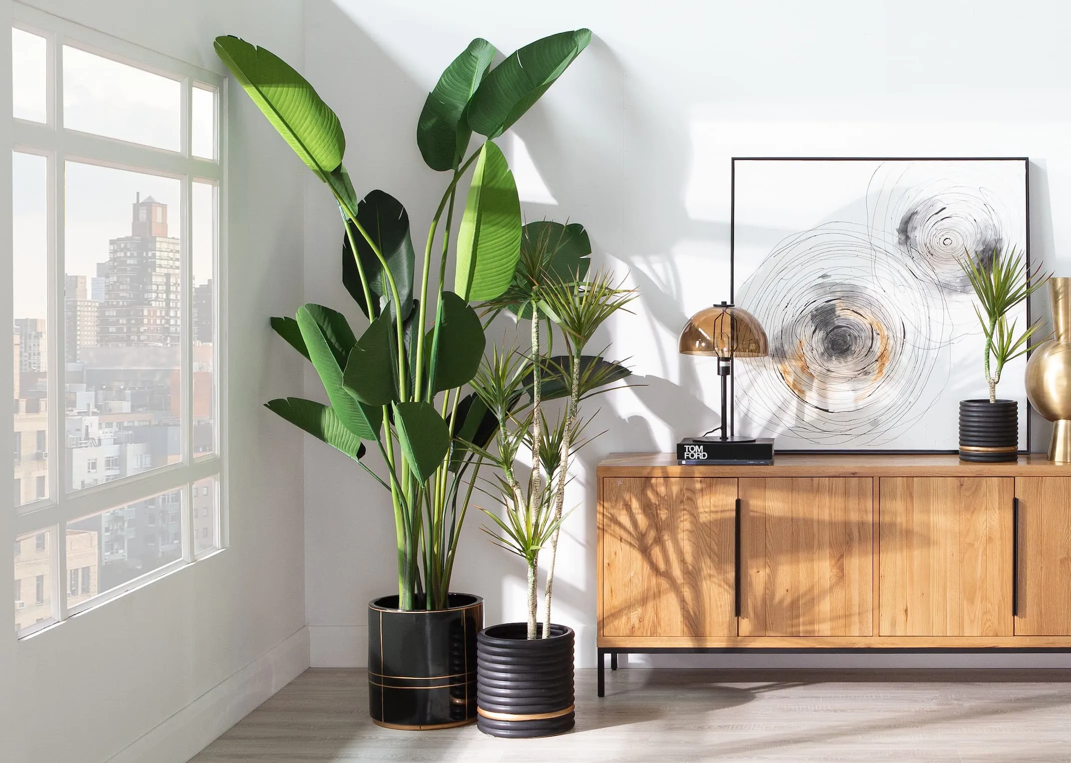 A lifestyle image of the Recap Sideboard with Strelitizia plant & yucca plant on the sideboard with Mella lamp