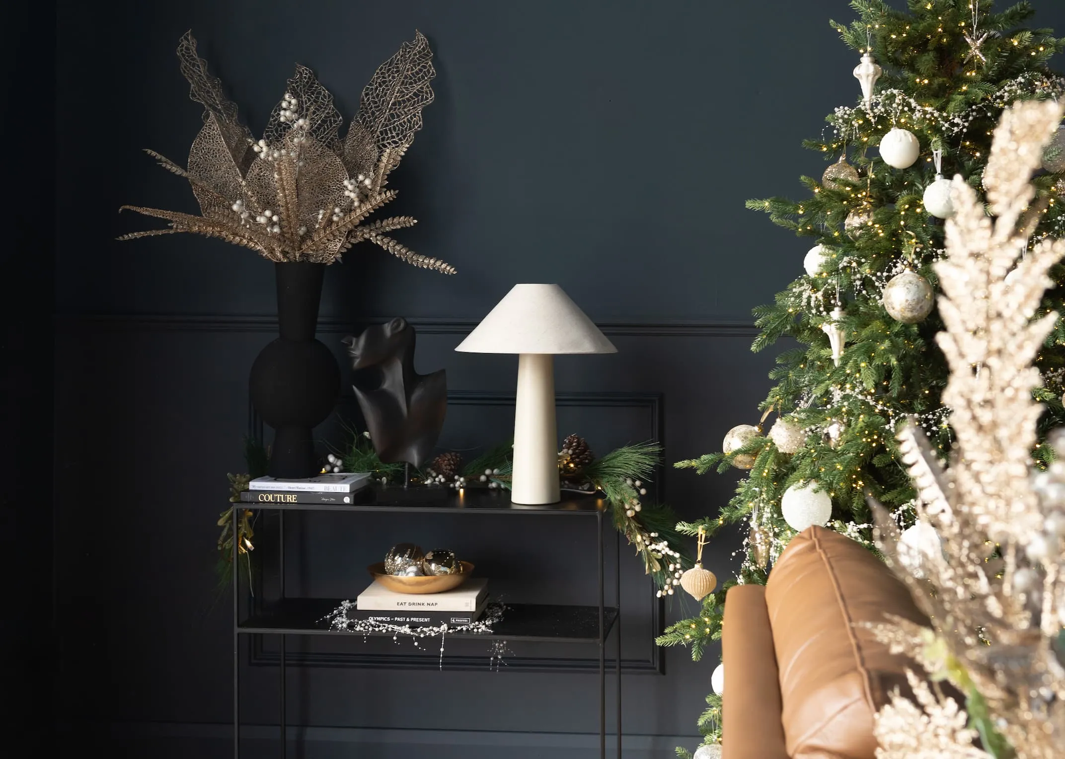 A lifestyle image of a Christmas tree decorated with gold spray and a pebble console with saturn lamp and kavandu vase with a selection of gold leaf picks