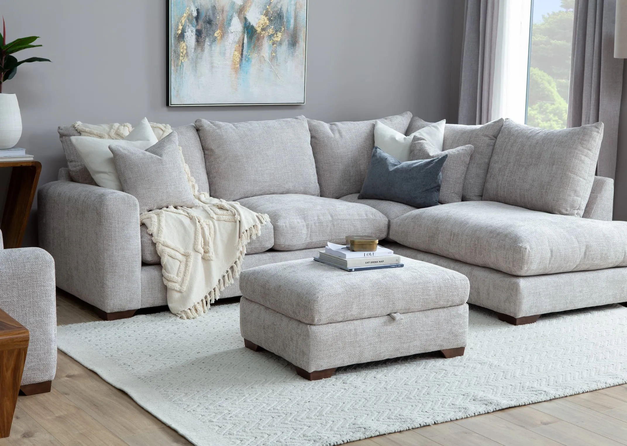 A lifestyle image of the Aurora footstool with the Corner sofa & Abstract print