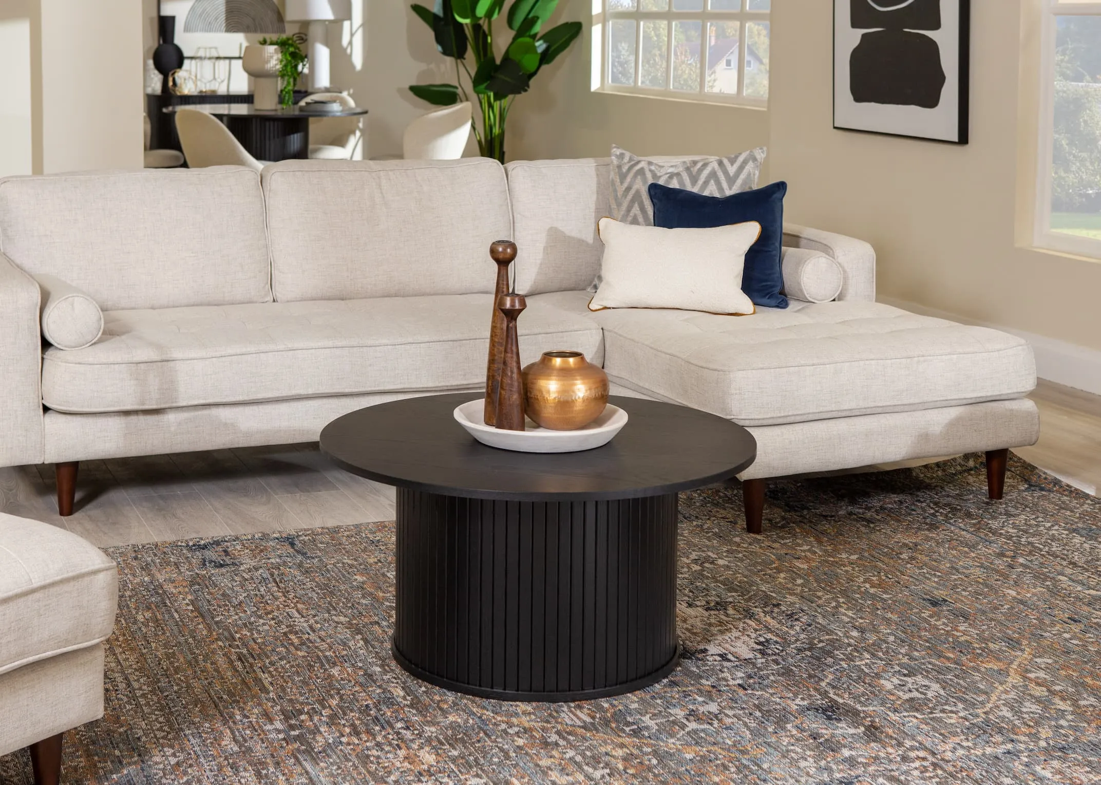 A lifestyle image of the Nola black oak round coffee table with couzana marble dish & tanana candleholders