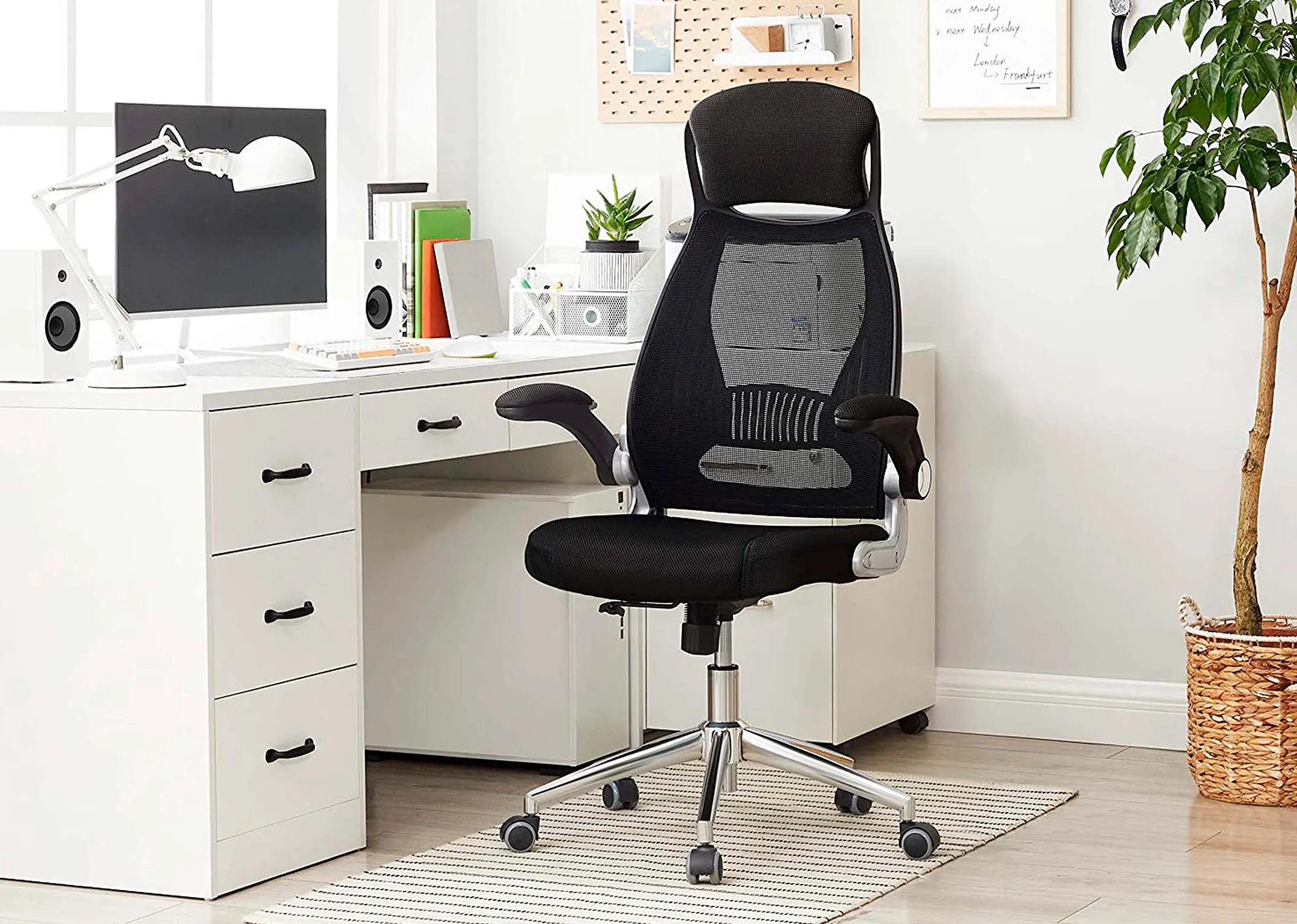 A lifestyle image of the Enigma Swivel Chair with a white desk with screens and a plant in an airy environment.
