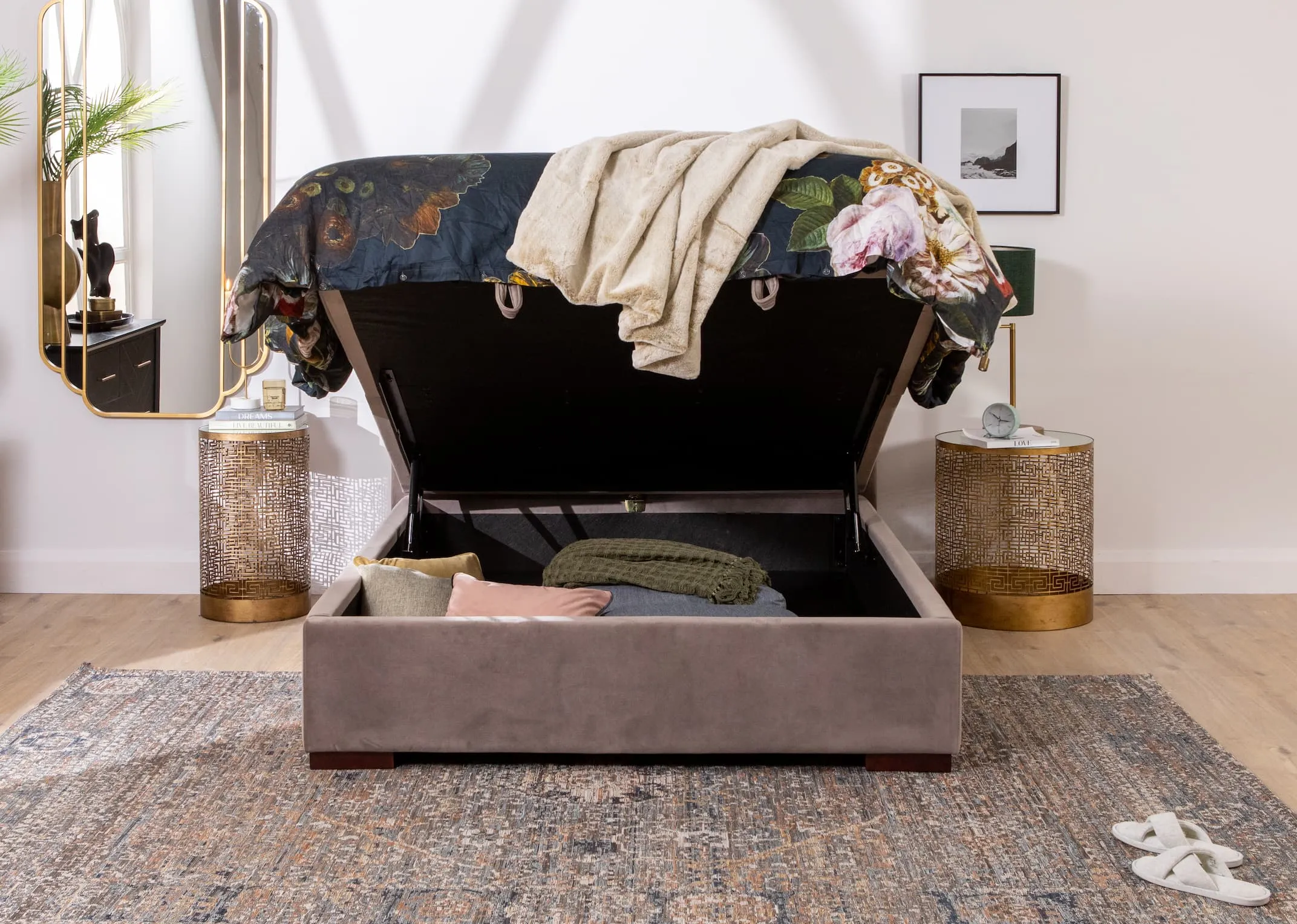 A lifestyle image of the Majestic taupe bed open to reveal under bed storage and chevron black chest of drawers