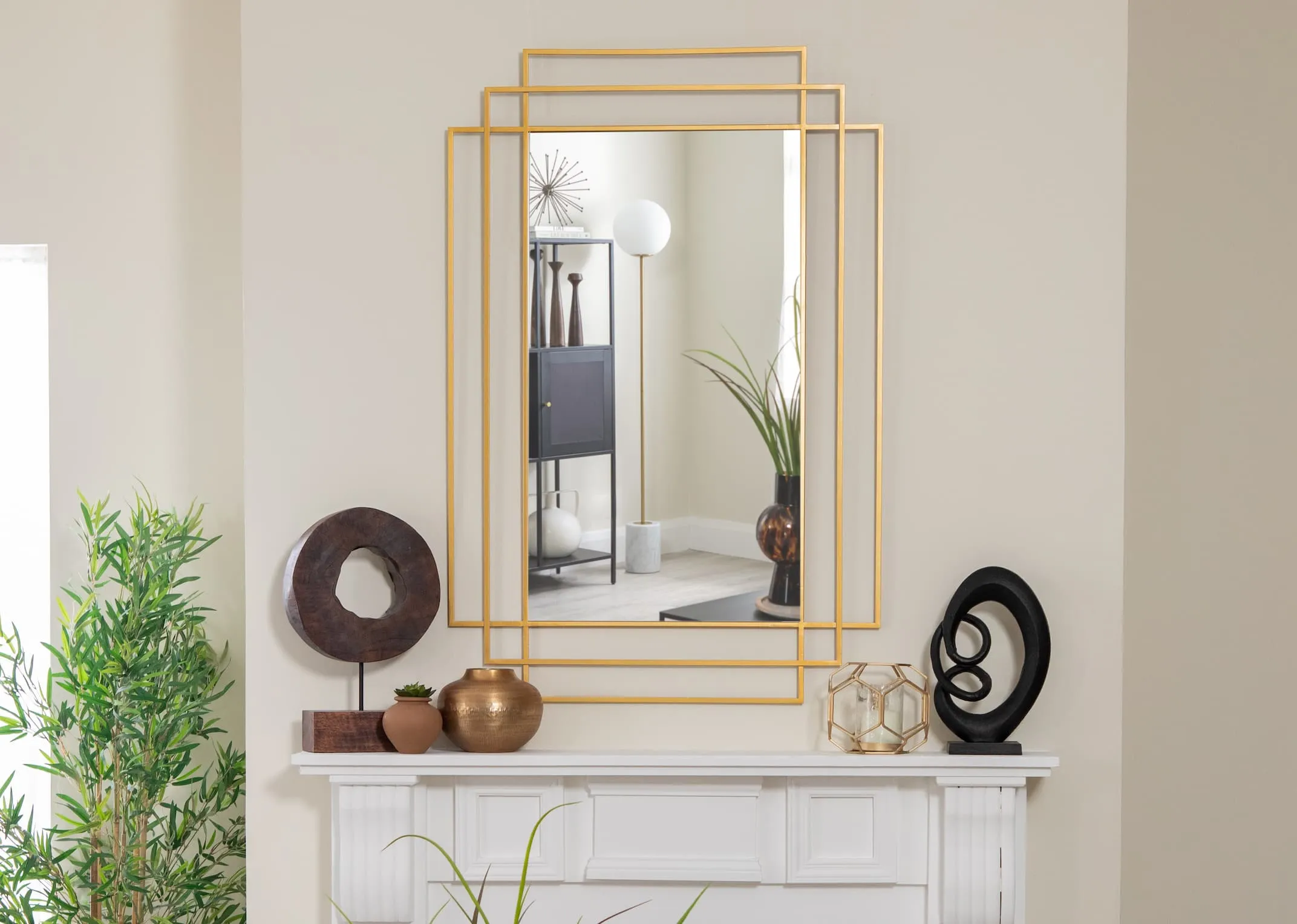 A lifestyle image of the Reine Gold mirror above a fireplace with gold vases and abstract ornament