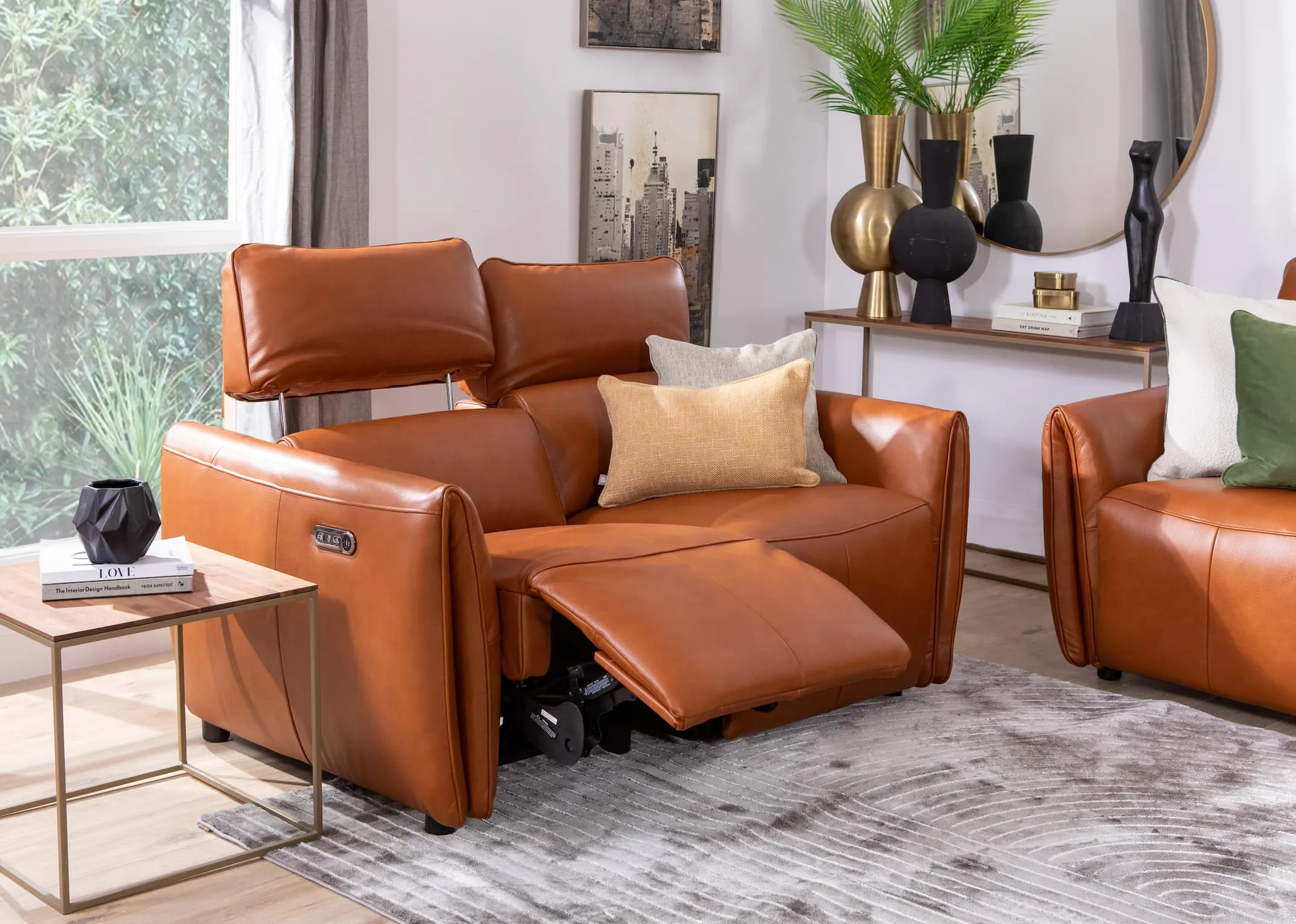A lifestyle image of the Icon sofa range with 2 seater reclined with gold & cream cushions with Frida rug and Aston tables