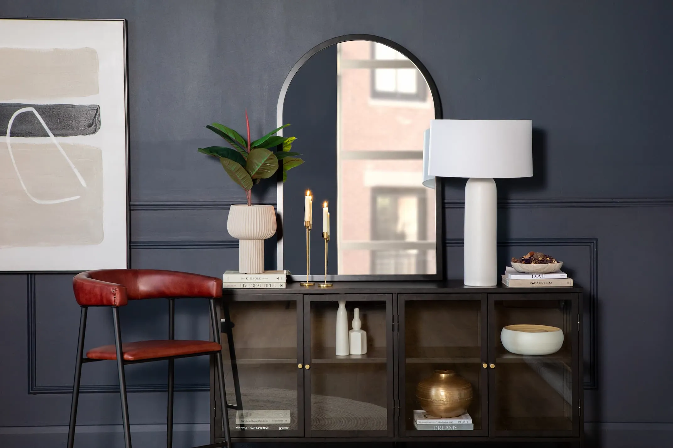A lifestyle image of the Carmel Cabinet with Chrisley mirror and Saturn lamp with Cuban stool