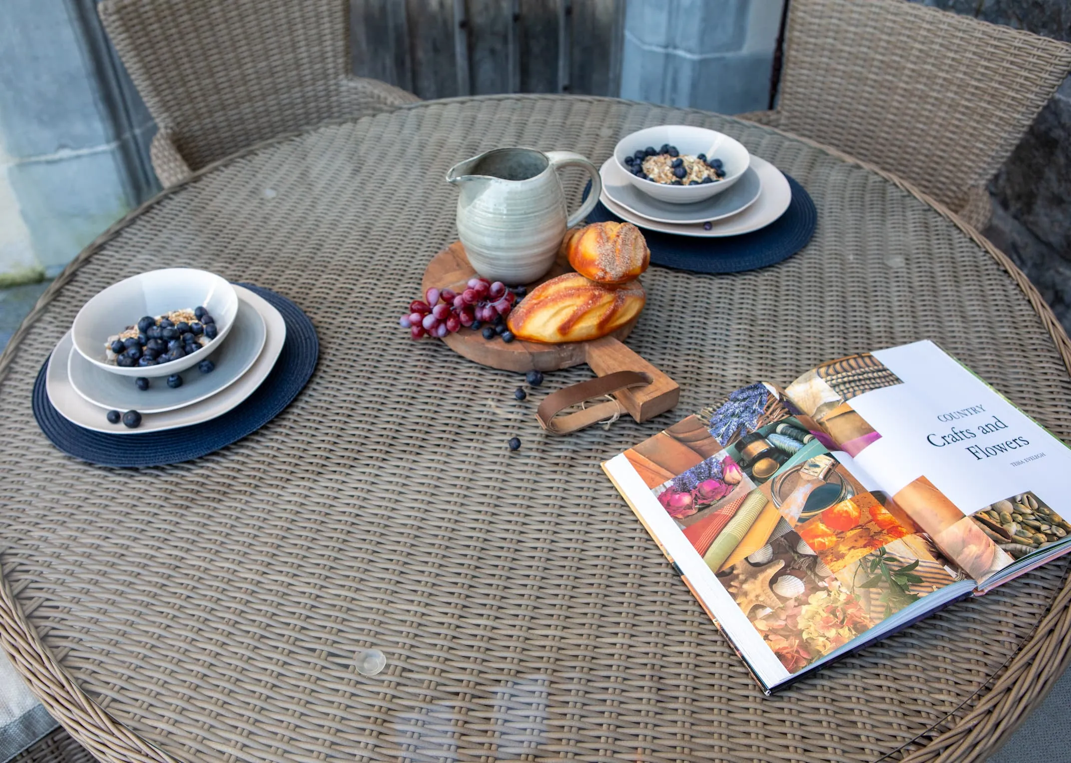 A lifestyle image of the Seville Round table with 4 round back chairs in  garden setting.