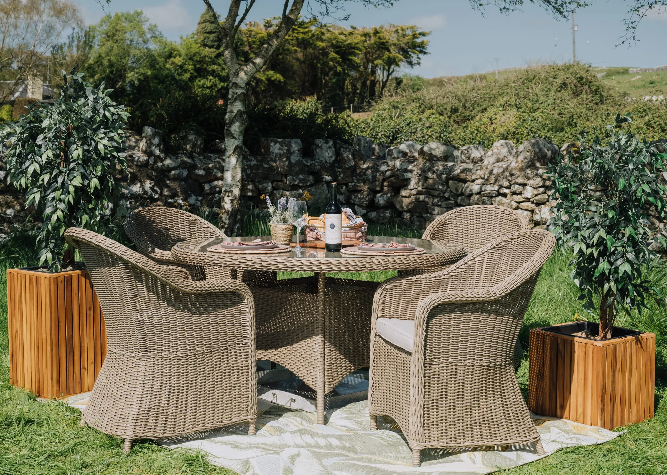A lifestyle image of the Seville Round table with 4 round back chairs in garden setting.