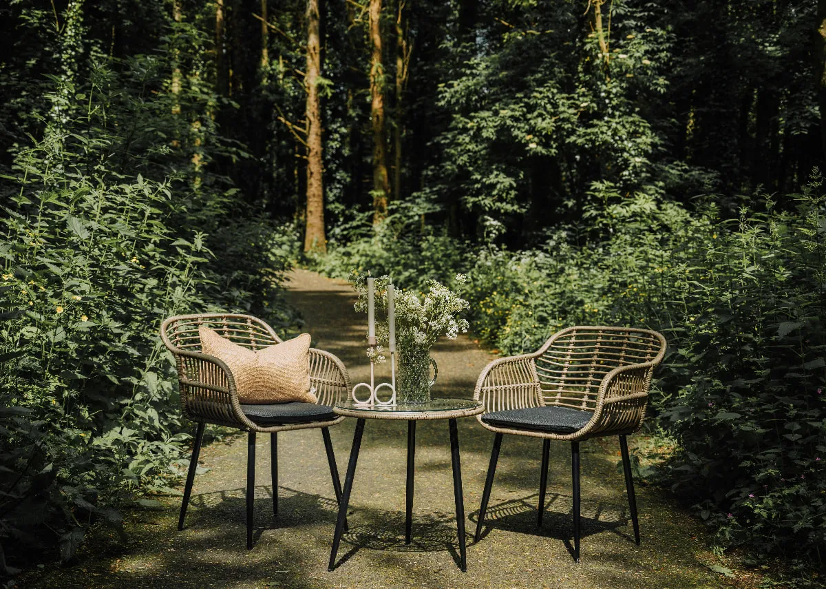 A bistro set with 2 wicker chairs and a small glass table from EZ Livings Menorca range. Angled view of rattan chair with metal legs