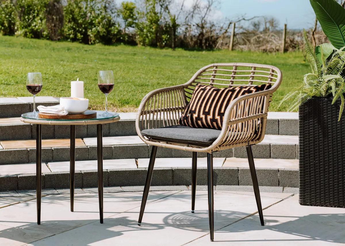 A lifestyle image of the Menorca set of 2 chairs and table with cushions in a forest landscape.