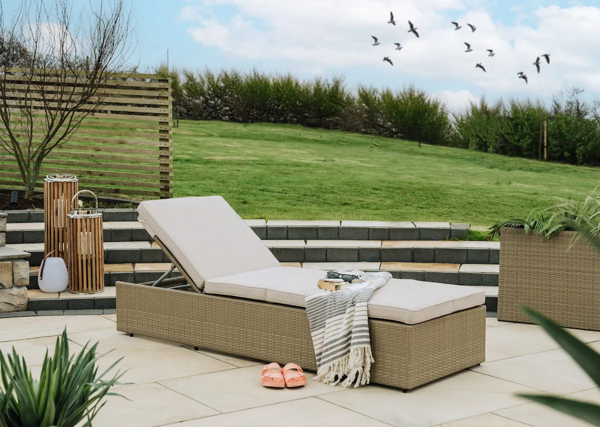 A light brown wicker sunlounger with fabric cushion removed from EZ Livings Granada range. Angled view of sunlounger with headrest lifted.