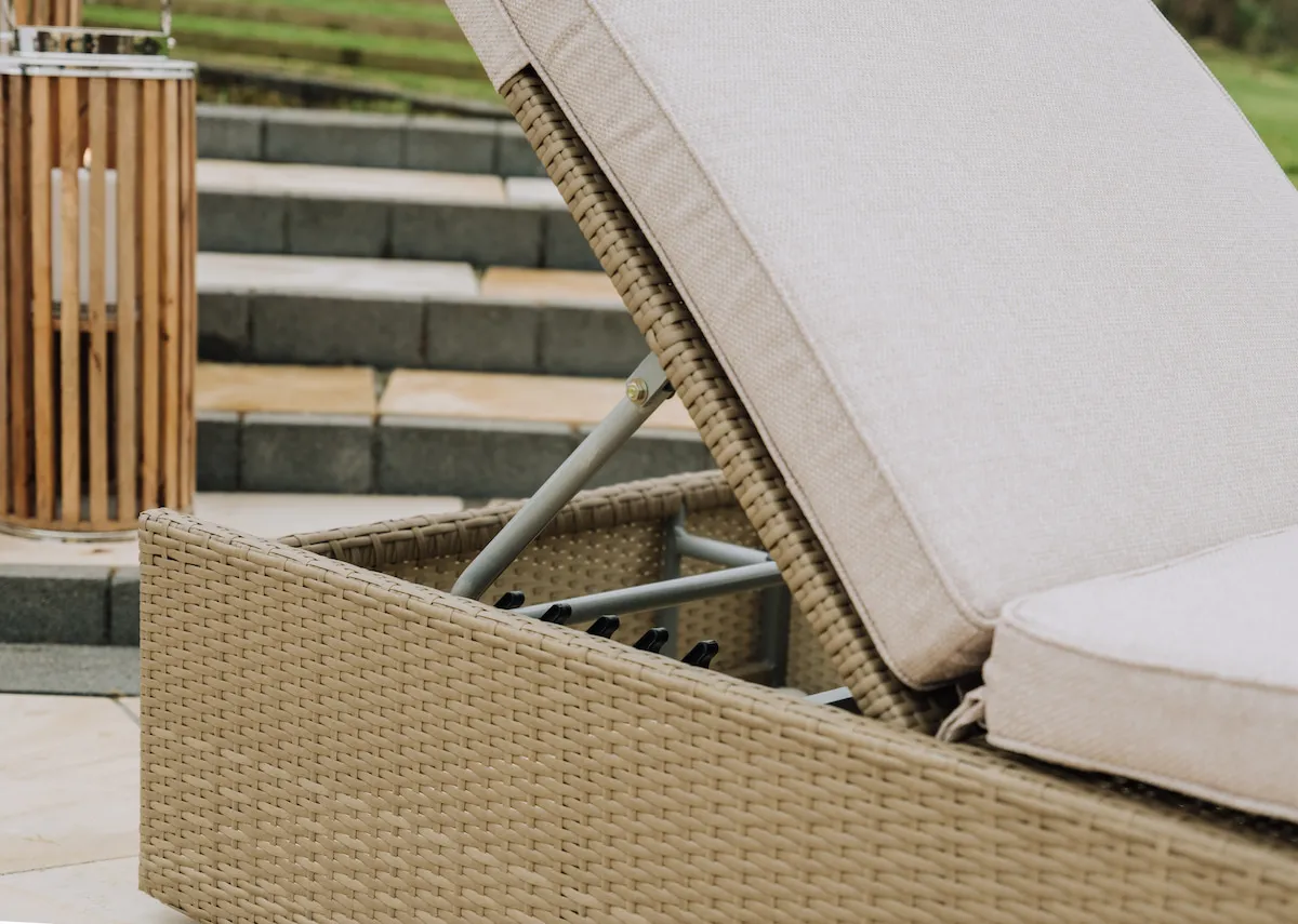 A light brown wicker sunlounger with beige fabric cushion from EZ Livings Granada range. Angled view of headrest down so sunlounger is flat.