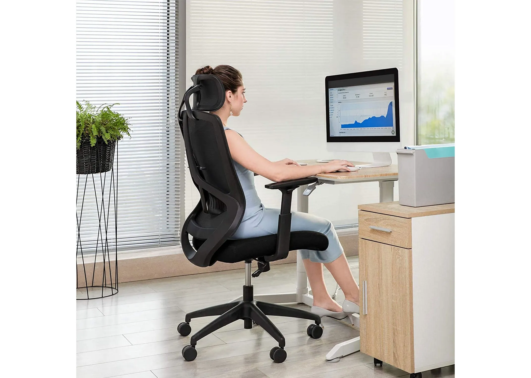 A black office chair from EZ Livings Redford range in a lifestyle image with a female sitting at a desk
