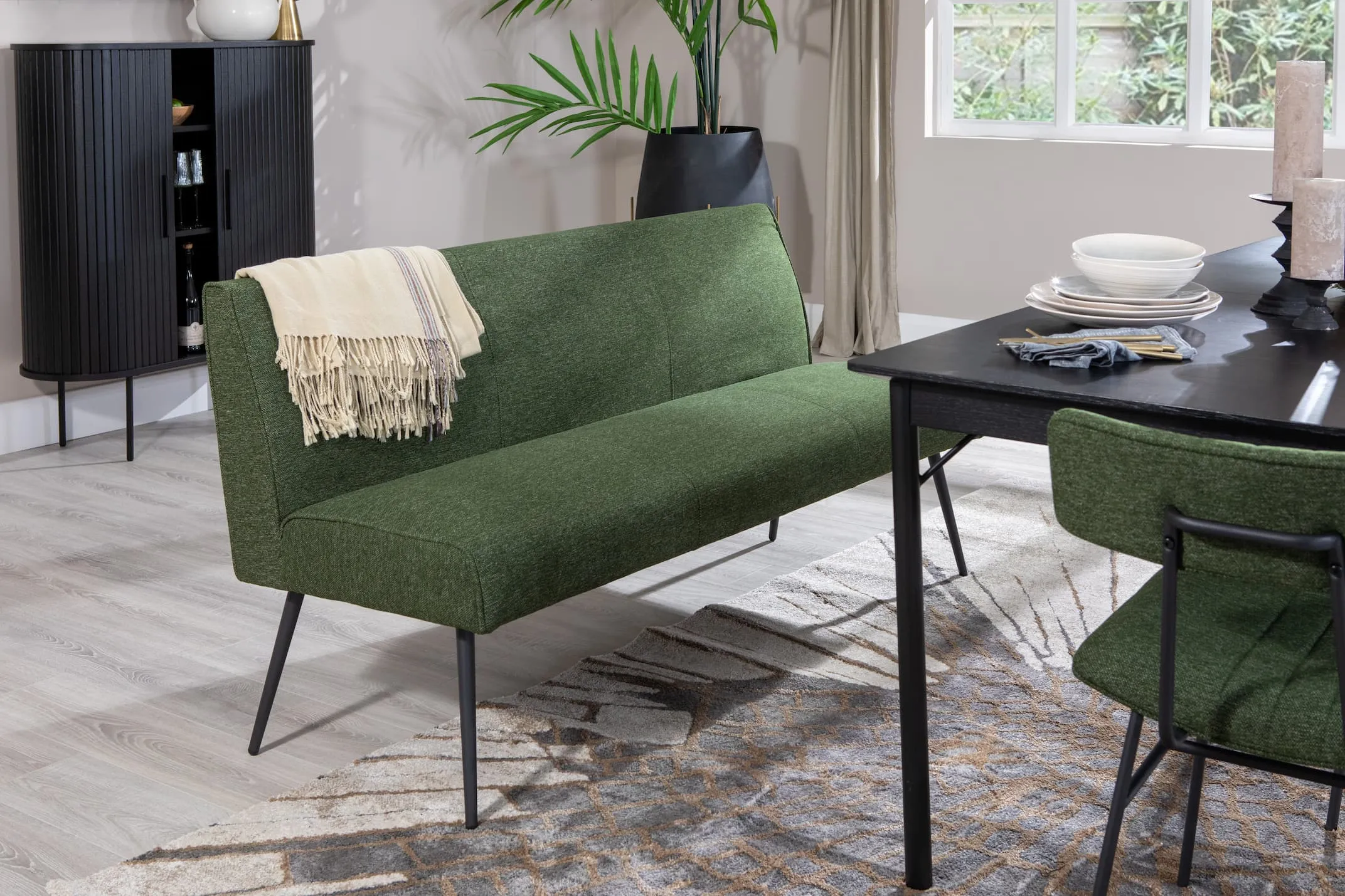 A lifestyle image of the Savona rectangular table with Decker green fabric bench & chairs and pasha rug with nola cabinet.