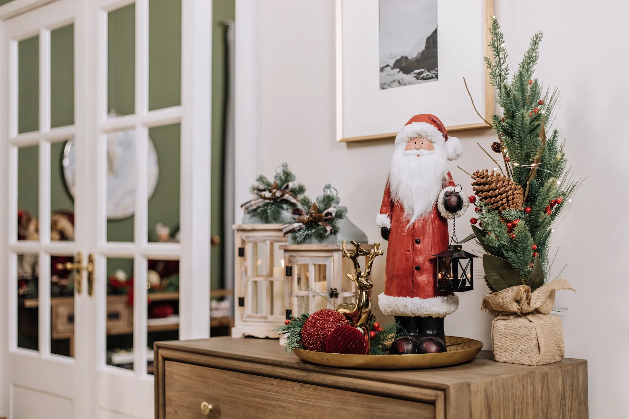 A lifetsyle image of a sideboard with wooden lanterns and Red Santa with Sparkle red bauble on gold dish.