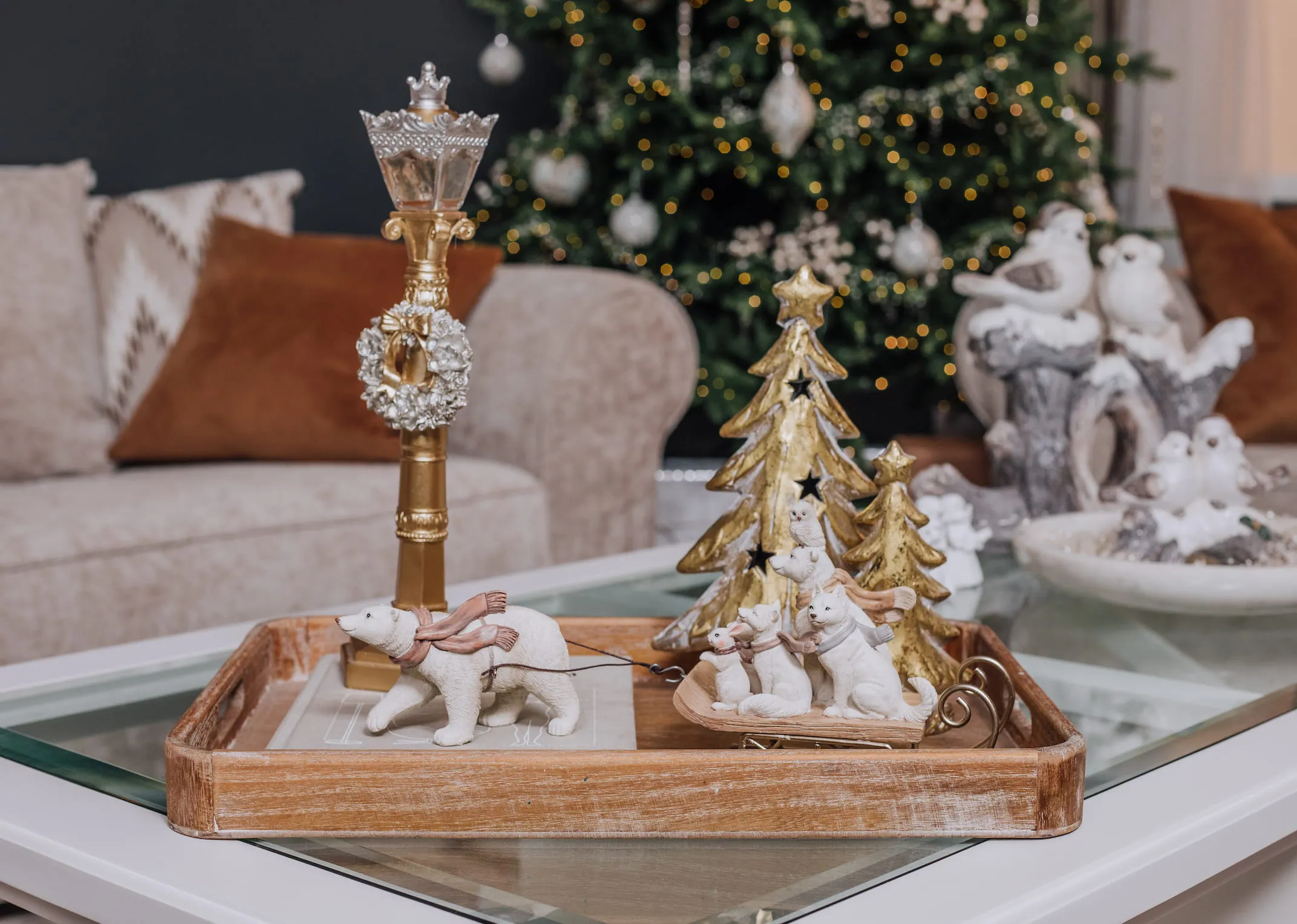 A lifestyle image of a tray on a coffee table with Polar bear with sled and a selection of gold trees & LED lamppost.