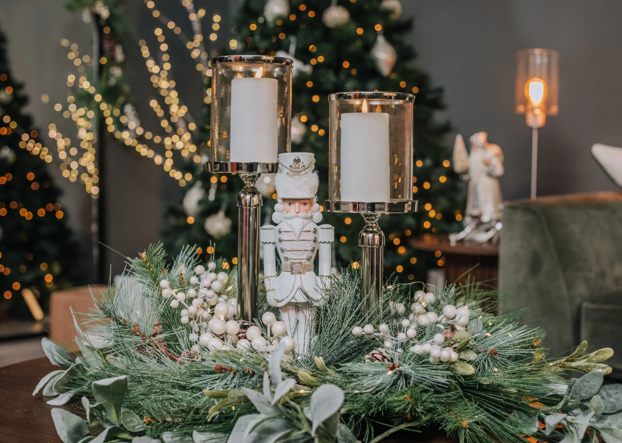 A lifestyle image of a festive pearl & pine wreath with White Nutcracker and set of glass candle holders.