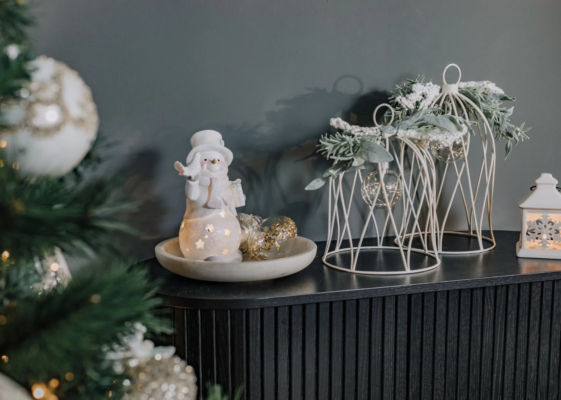 A lifestyle image of the Nola Black cabinet with Snowman with Doves and Wire Bells with White Lantern & candle lit.