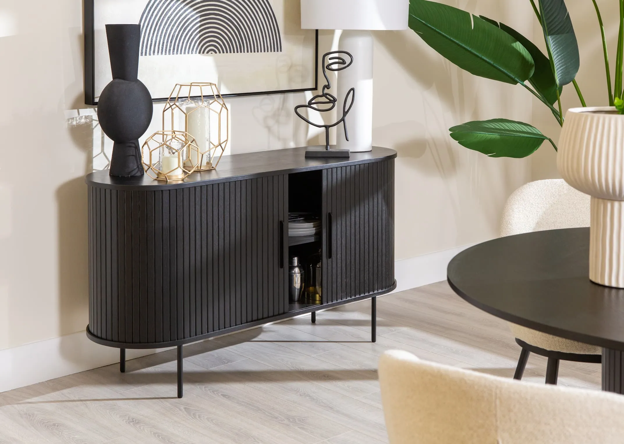 A lifestyle image of the Nola sideboard in black open to reveal storage space with kavandu vase and gold lanterns