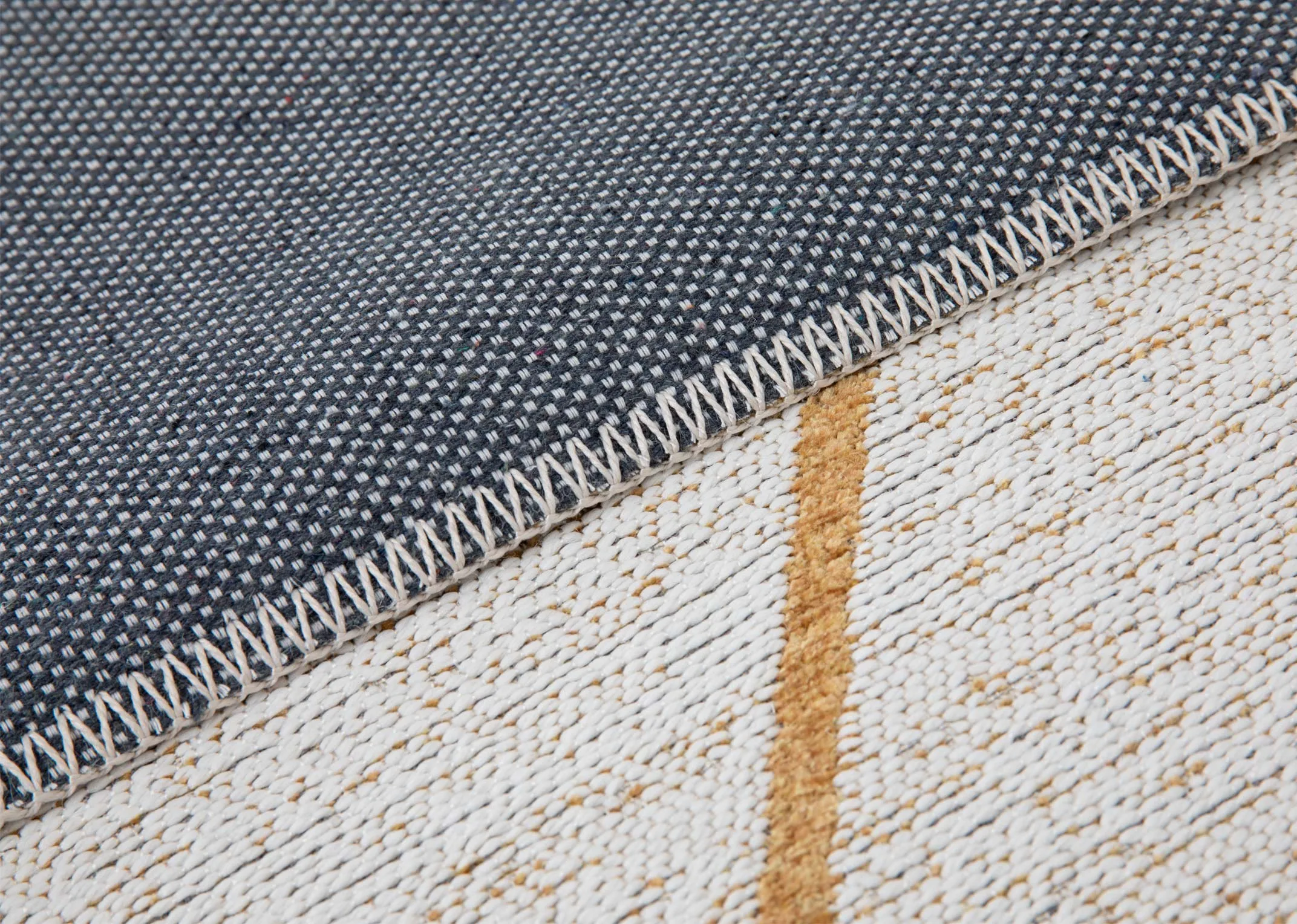 A large white rug with gold linear pattern from EZ Livings Charvi range.. Closeup of blue underlay and woven light texture
