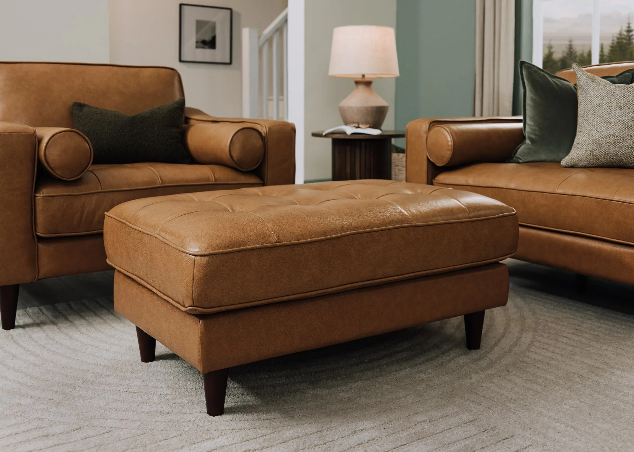 A lifestyle image of the Genoa tan leather footstool with armchair and nola side table with Mai lamp.
