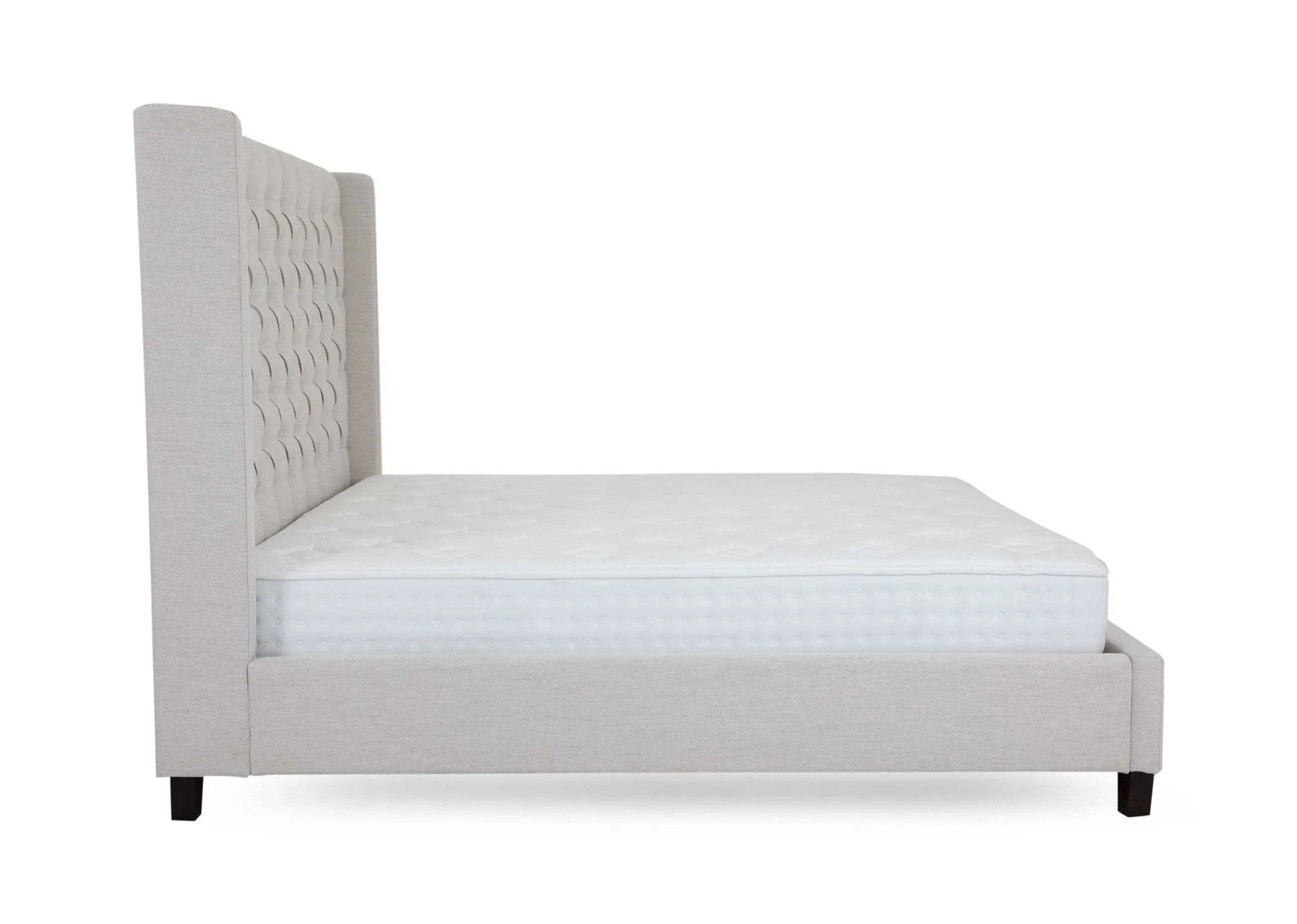 A cream fabric bedframe with high tufted headboard from EZ Livings Enhance range. A side view of the winged headboard and dark feet.