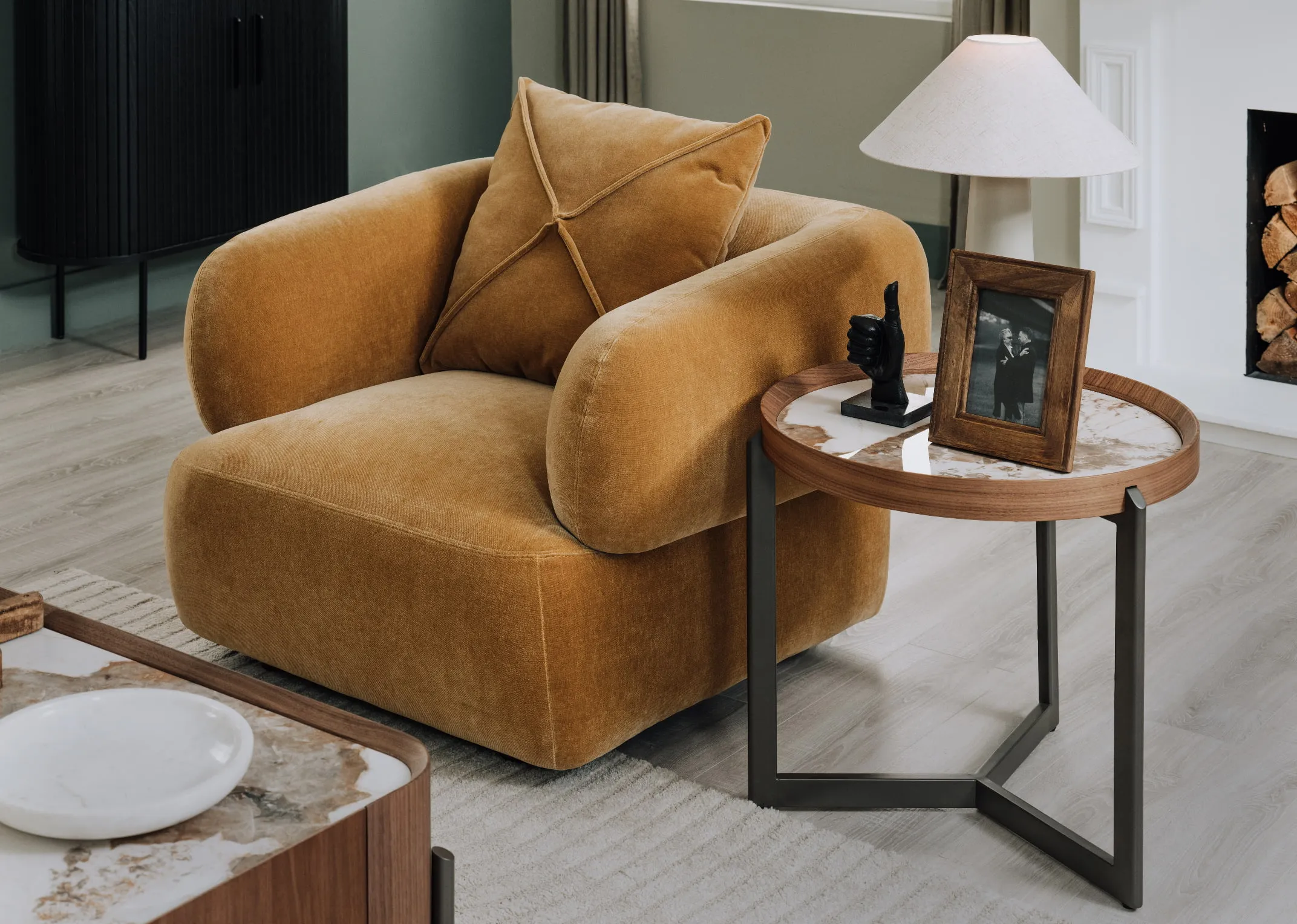 A lifestyle image of the Carla gold armchair with century round side table with wood frame and Daisy lamp.