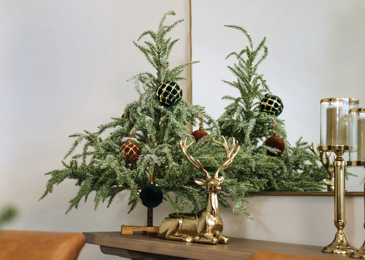 A lifestyle image of the Miracle tree with green and Santa baubles with gold lying deer ornaments