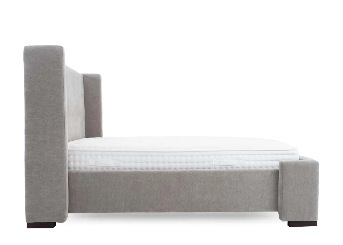 A grey fabric bed frame with high winged headboard from EZ Livings Quay west range. Side view of covered sides and dark feet