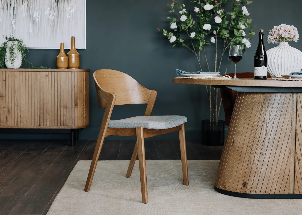 A lifestyle image of the Vega rustic dining chair with grey fabric seat with the oval dining table.