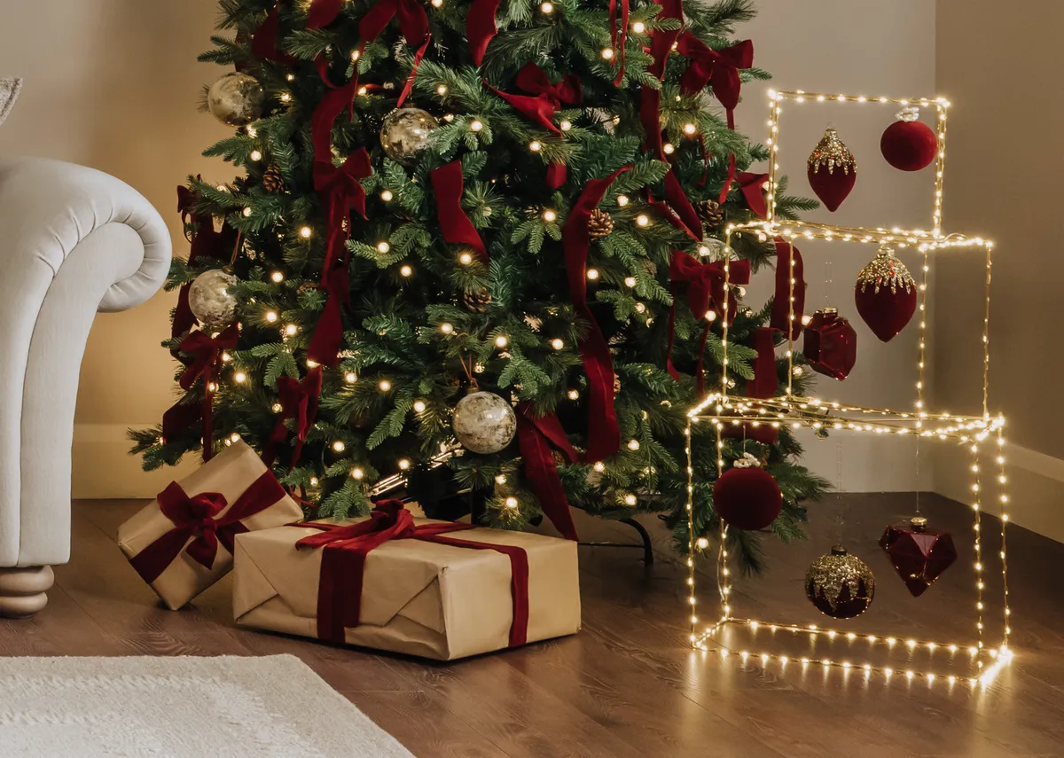 A lifestyle image of the Gold Gift box with Rockefeller christmas tree abd a selection of red and gold baubles