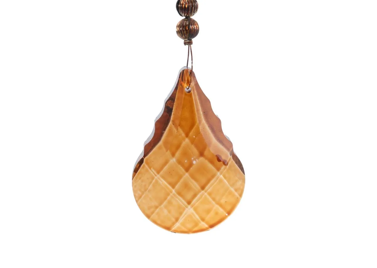 A close up of the large faceted amber colored crystal drop on a brass large crystal garland showing its intricate pattern.