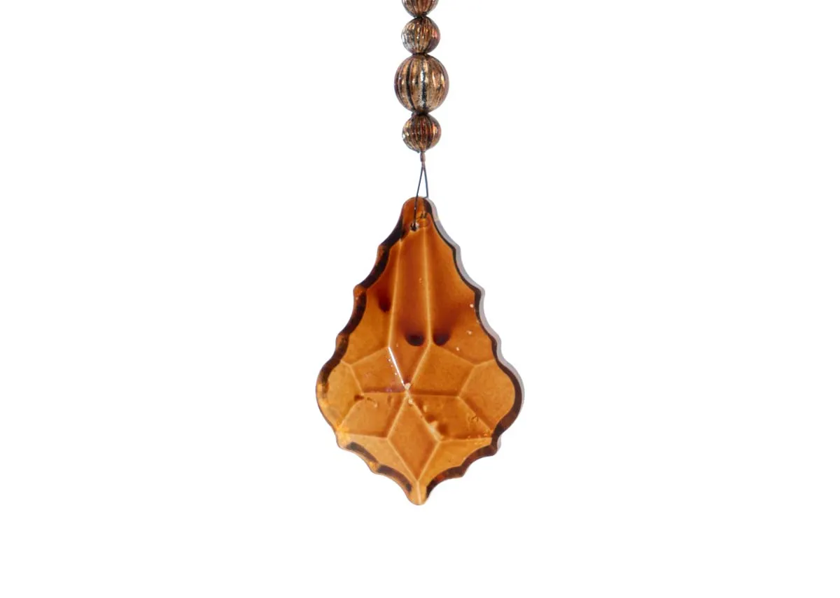 A close up of the small faceted amber colored crystal drop on a brass small crystal garland showing its intricate pattern.