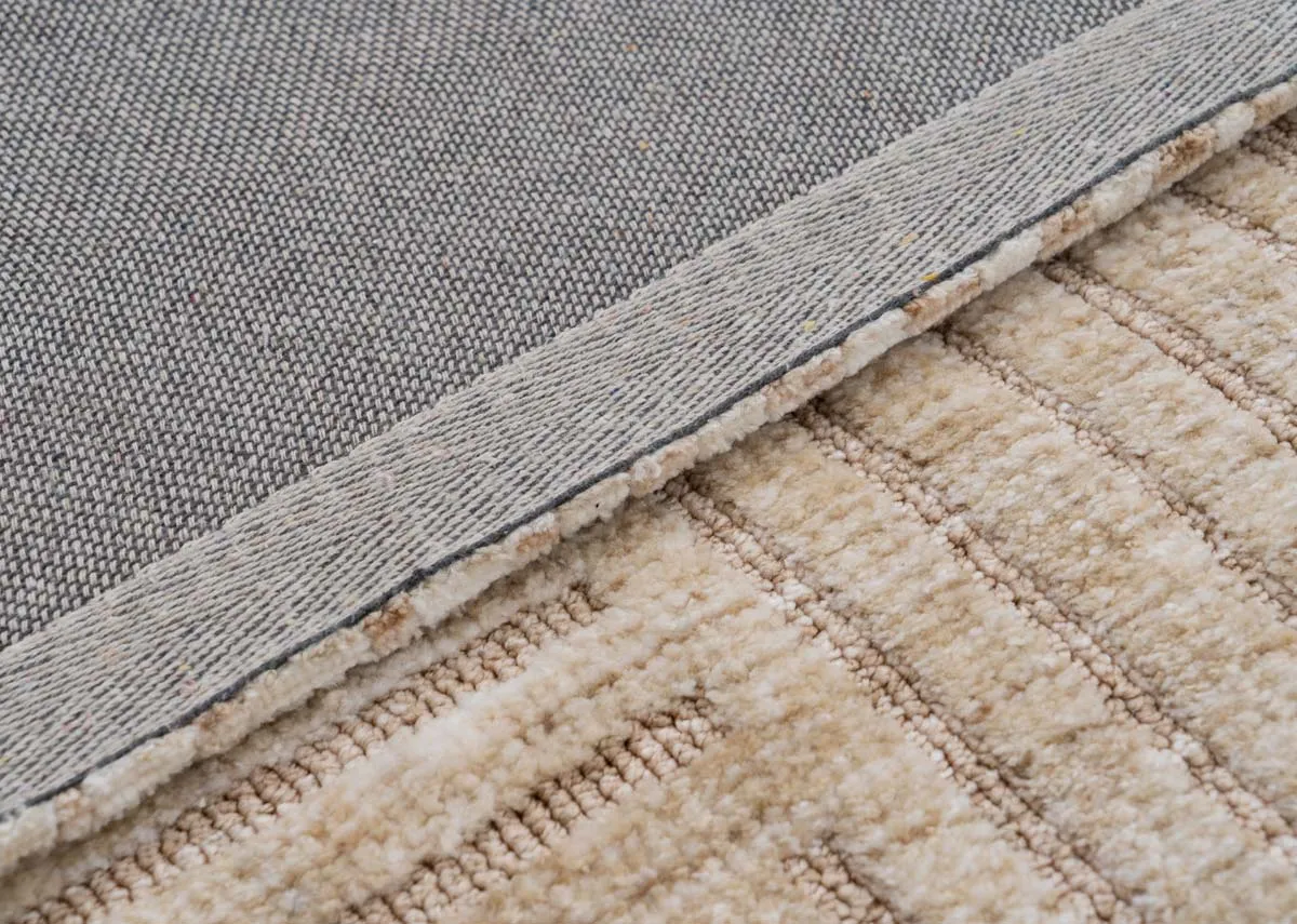 A close up showing the sand colored rugs textured top surface with a geometric pattern and its woven grey underside.