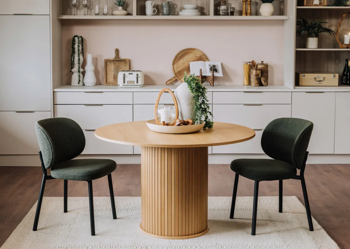 A lifestyle image of the Nola natural oak round dining table with swan chairs in green.