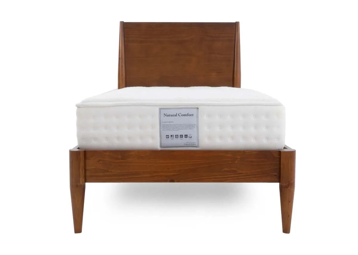 A wooden bed frame with a simple headboard and tapered legs supporting a white quilted mattress with a product label.