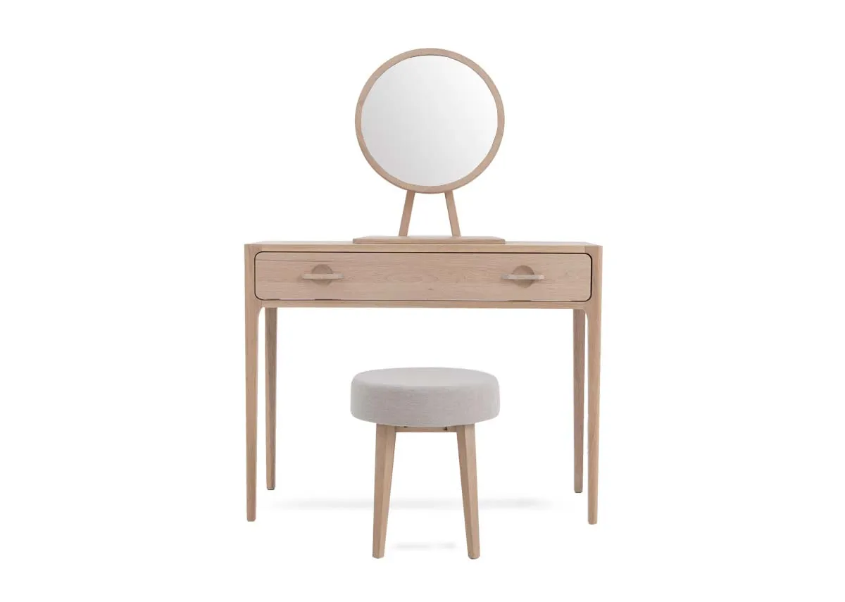 A white oak dressing table with 1 large drawer and round mirror with a grey fabric stool. Front view
