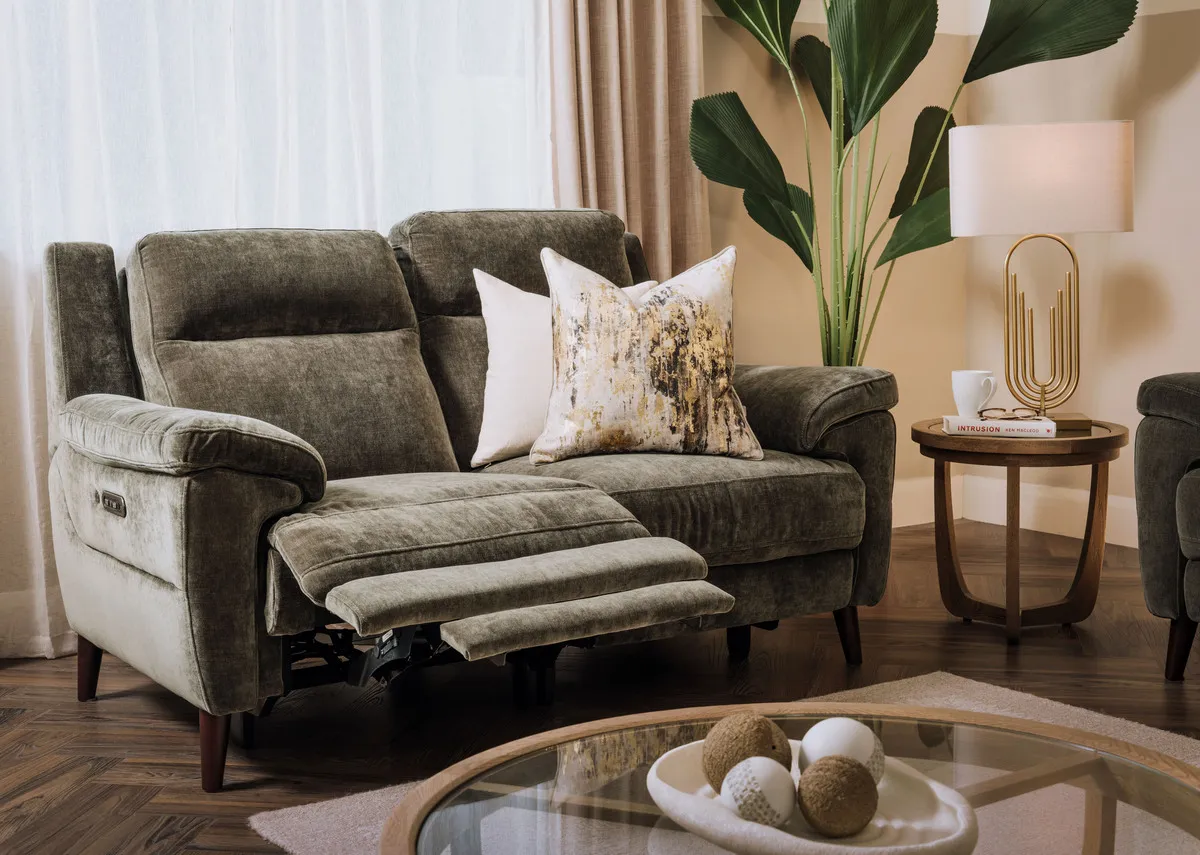 A lifestyle image of the Elliot green 2 seater sofa reclined with Alexis tables