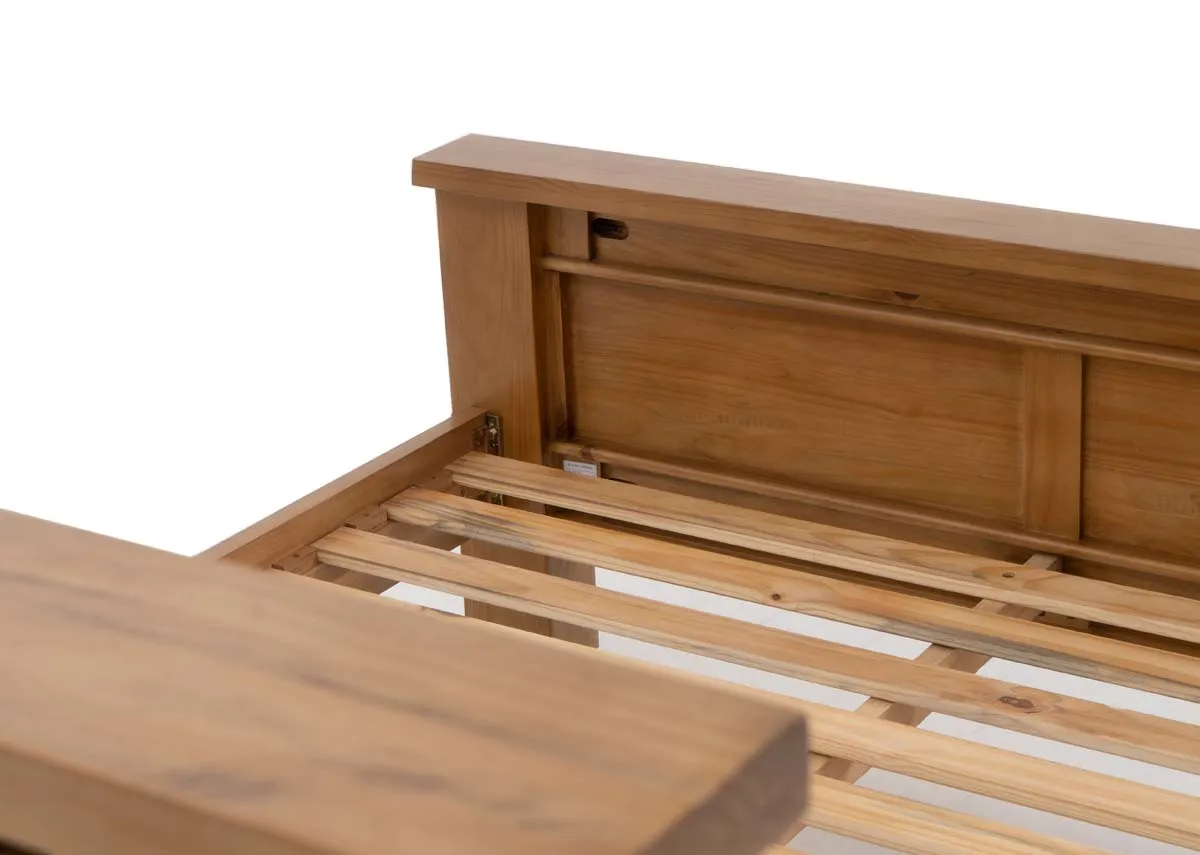 A close up of a thick wooden bed frame leg and the light wooden slats supporting a mattress.