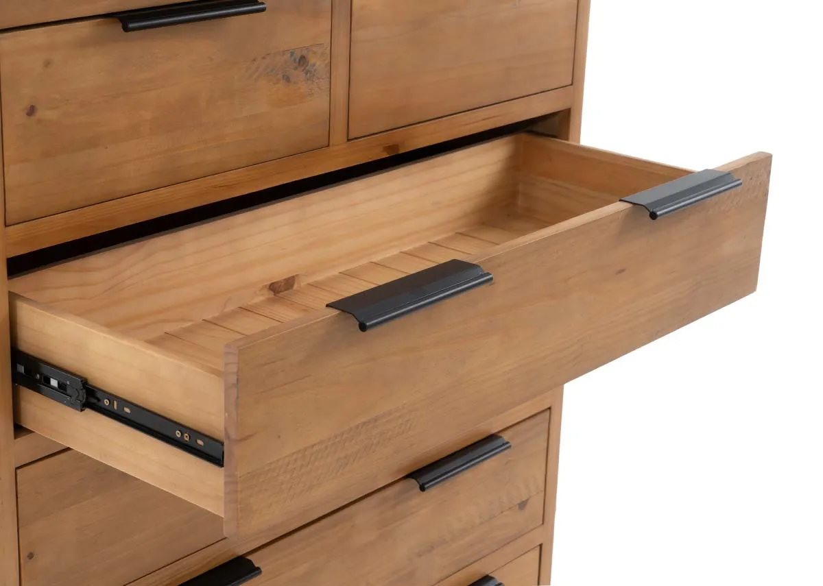 A close up of a larger open drawer in a light brown wooden tallboy showing the wooden interior and black handle.